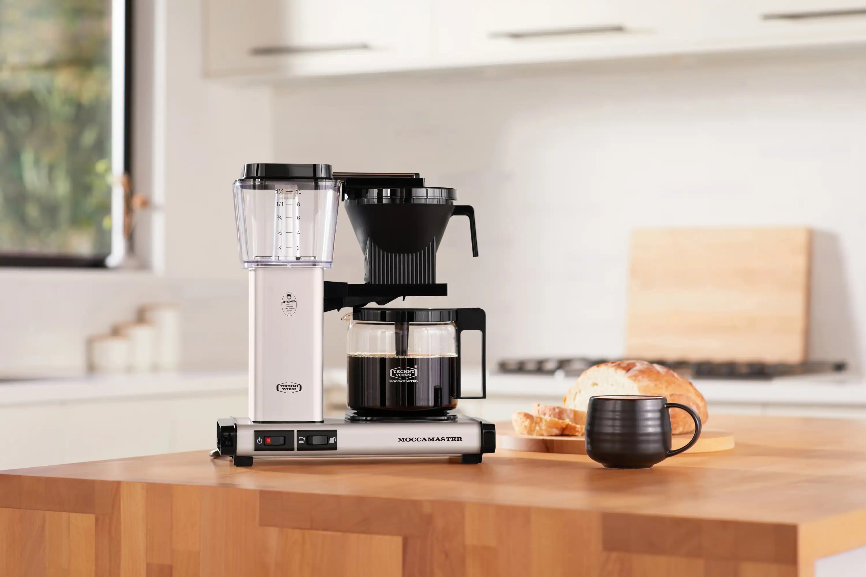 Matte silver coffee maker with glass carafe on countertop, black brew basket