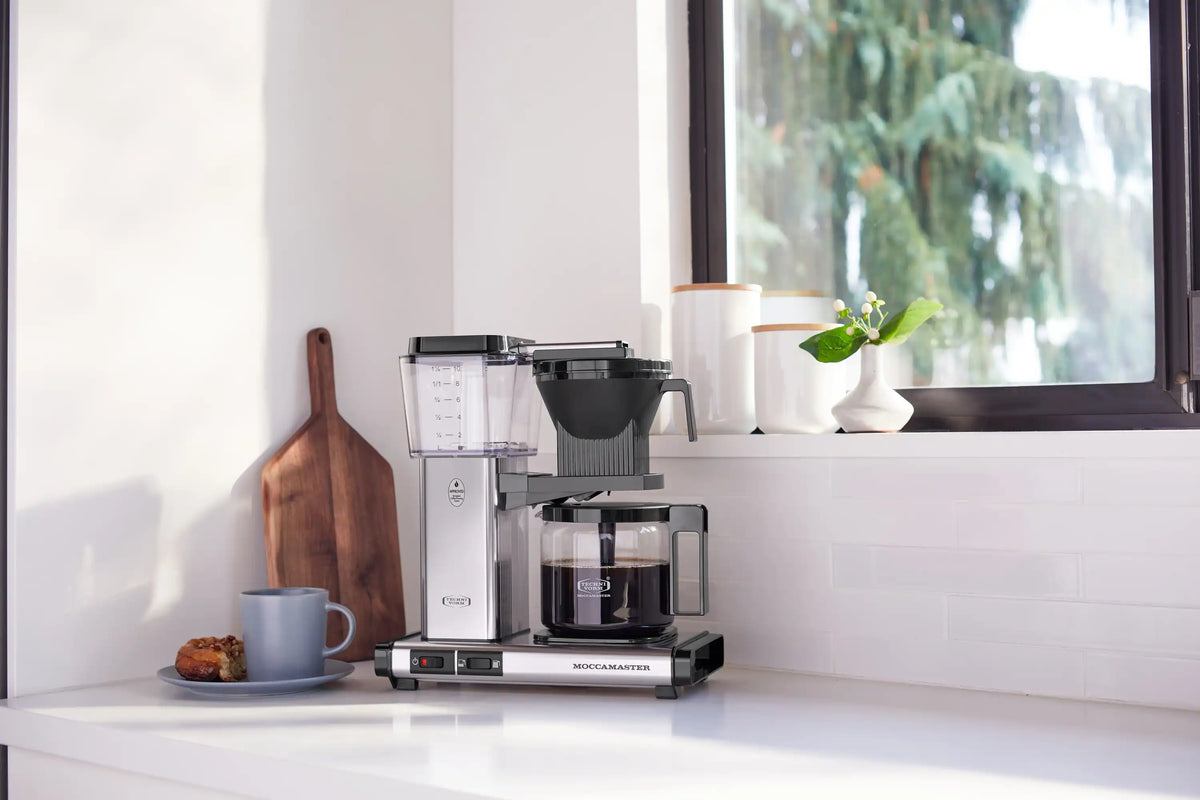 Moccamaster 10-cup coffee maker on counter with glass carafe and black brew basket.