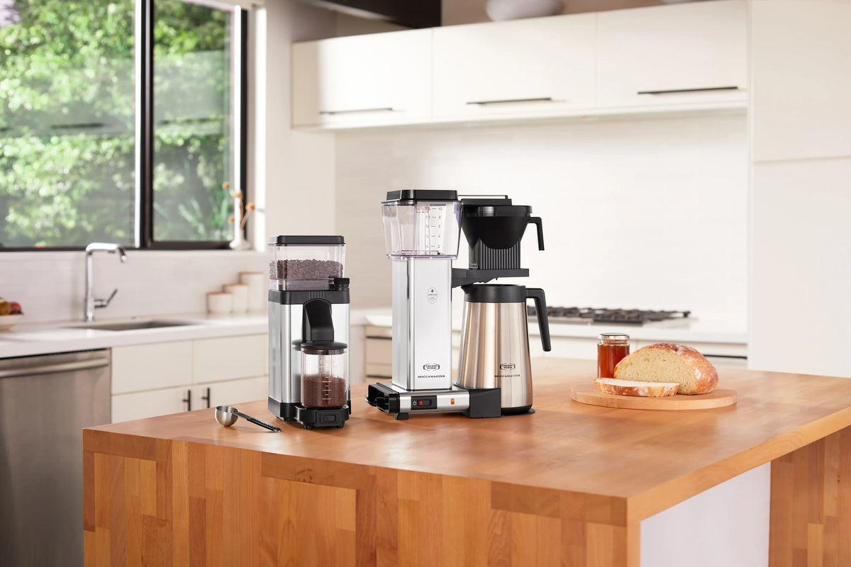Polished silver burr grinder with clear hopper, black chute, and countertop base