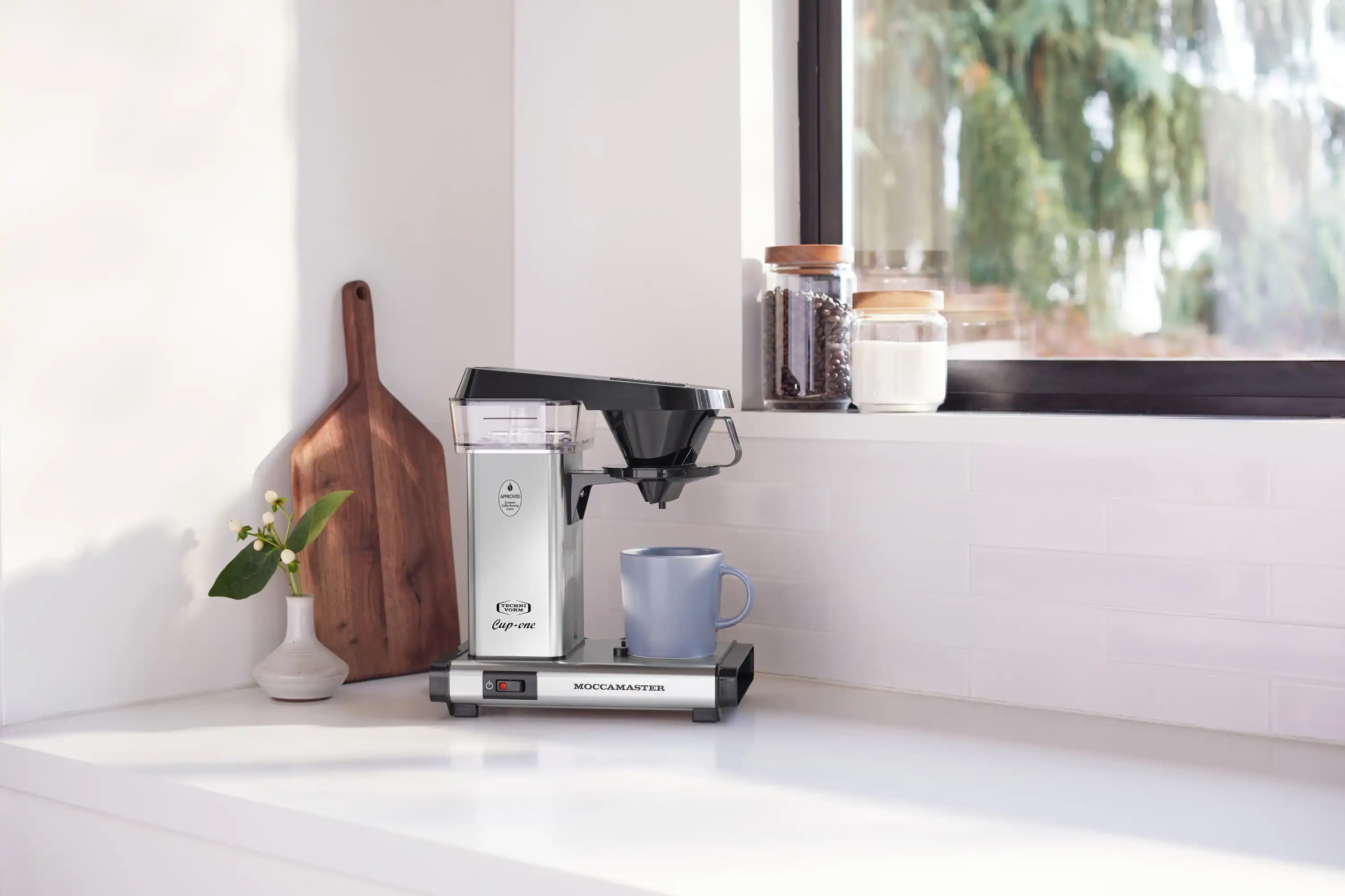 Single-cup coffee maker in polished silver with black funnel on countertop