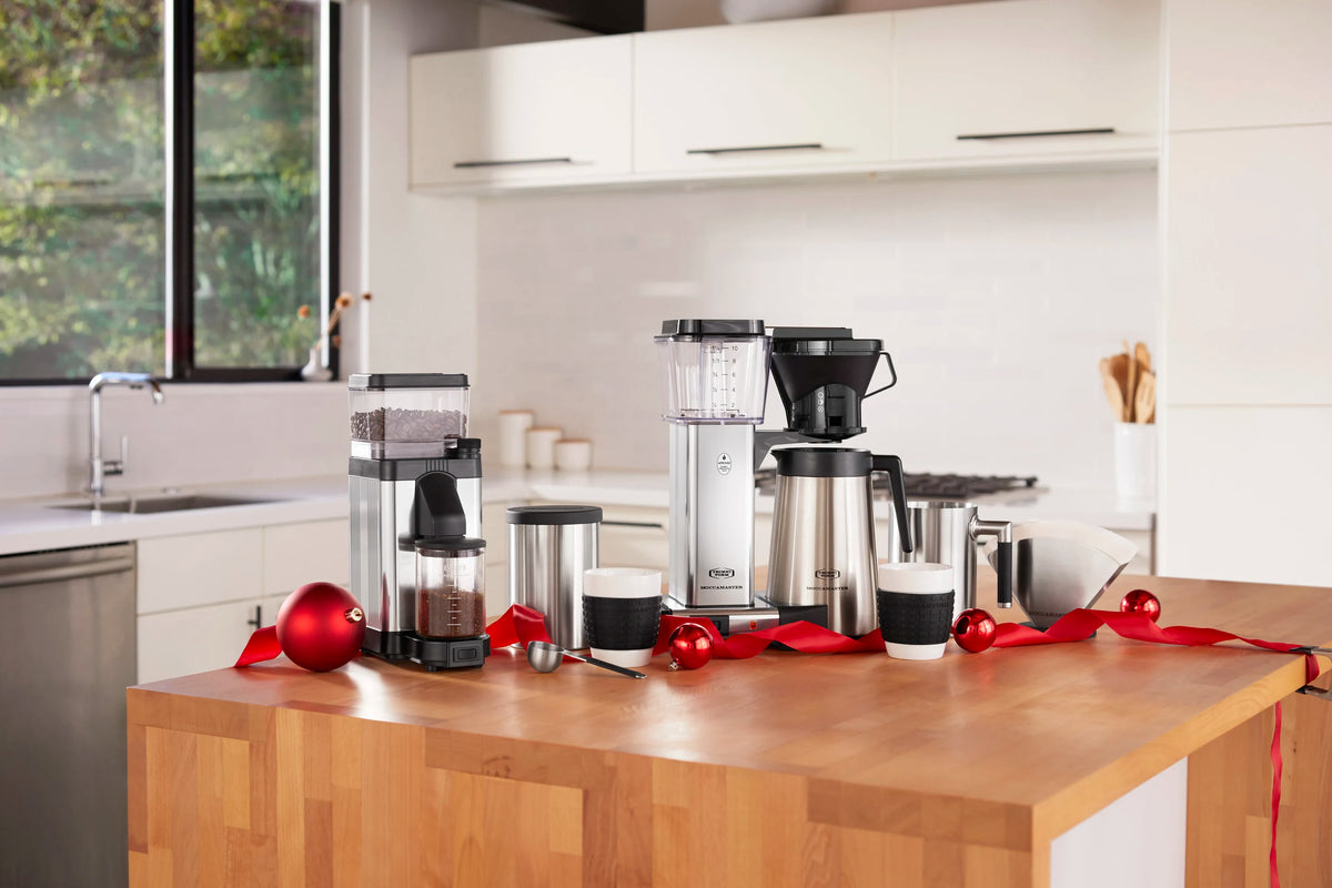Polished silver burr grinder with clear hopper and black base, holiday decor nearby