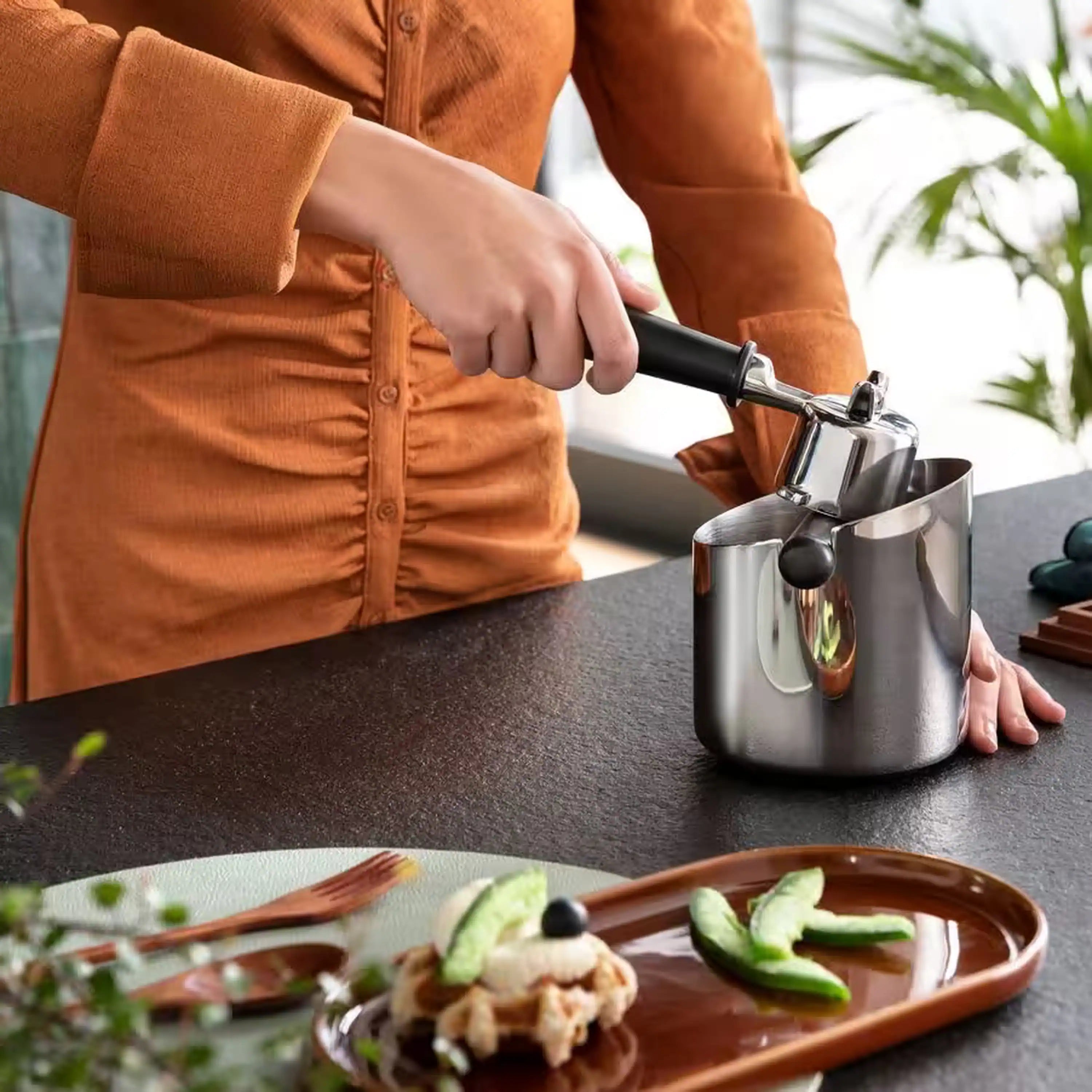 Stainless steel coffee knock box with black handle being used at countertop