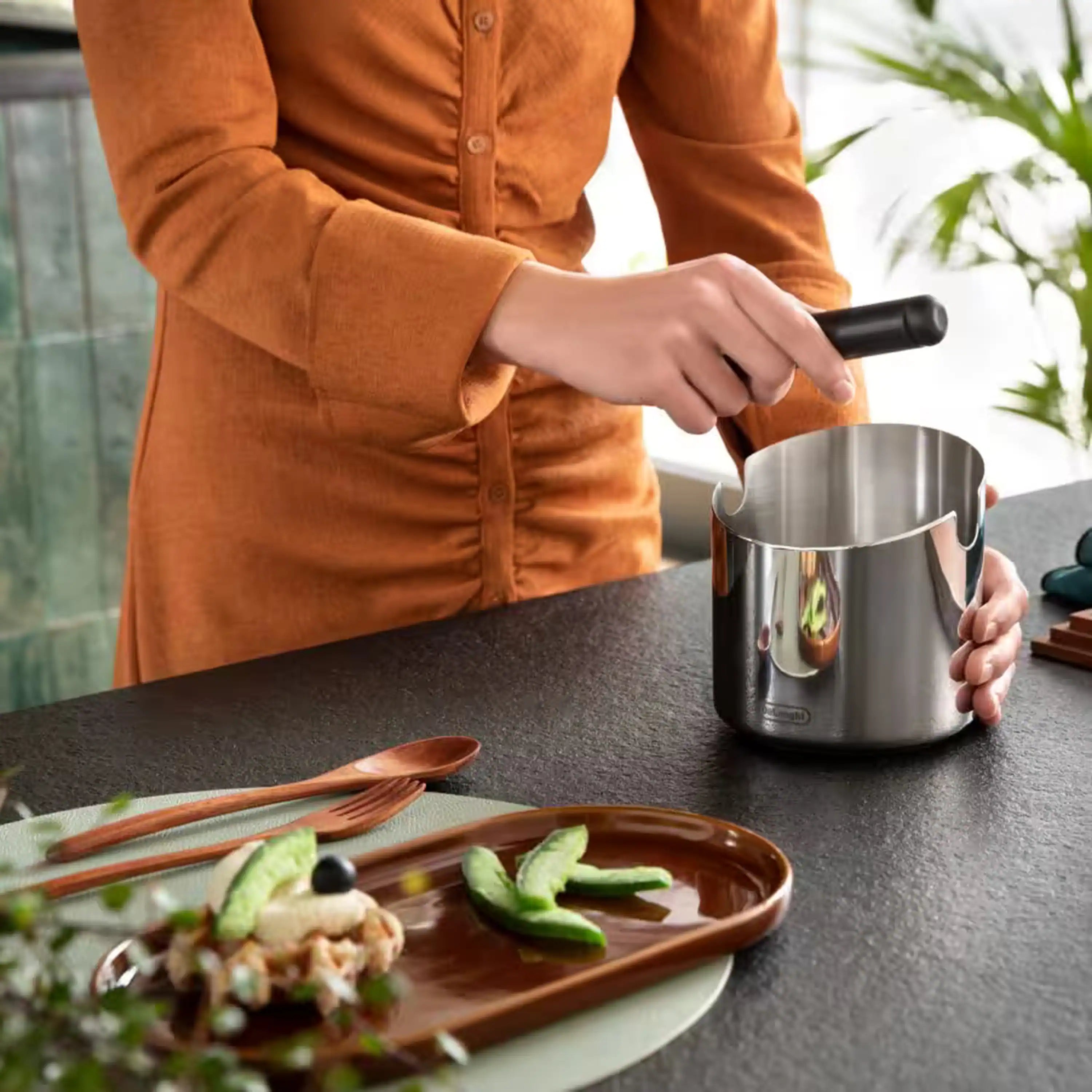Stainless steel coffee knock box with black handle and side spout, on countertop