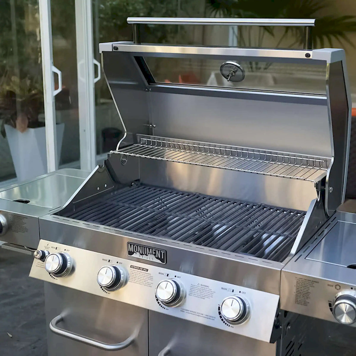 Open stainless steel gas grill with dark grates and wire warming rack