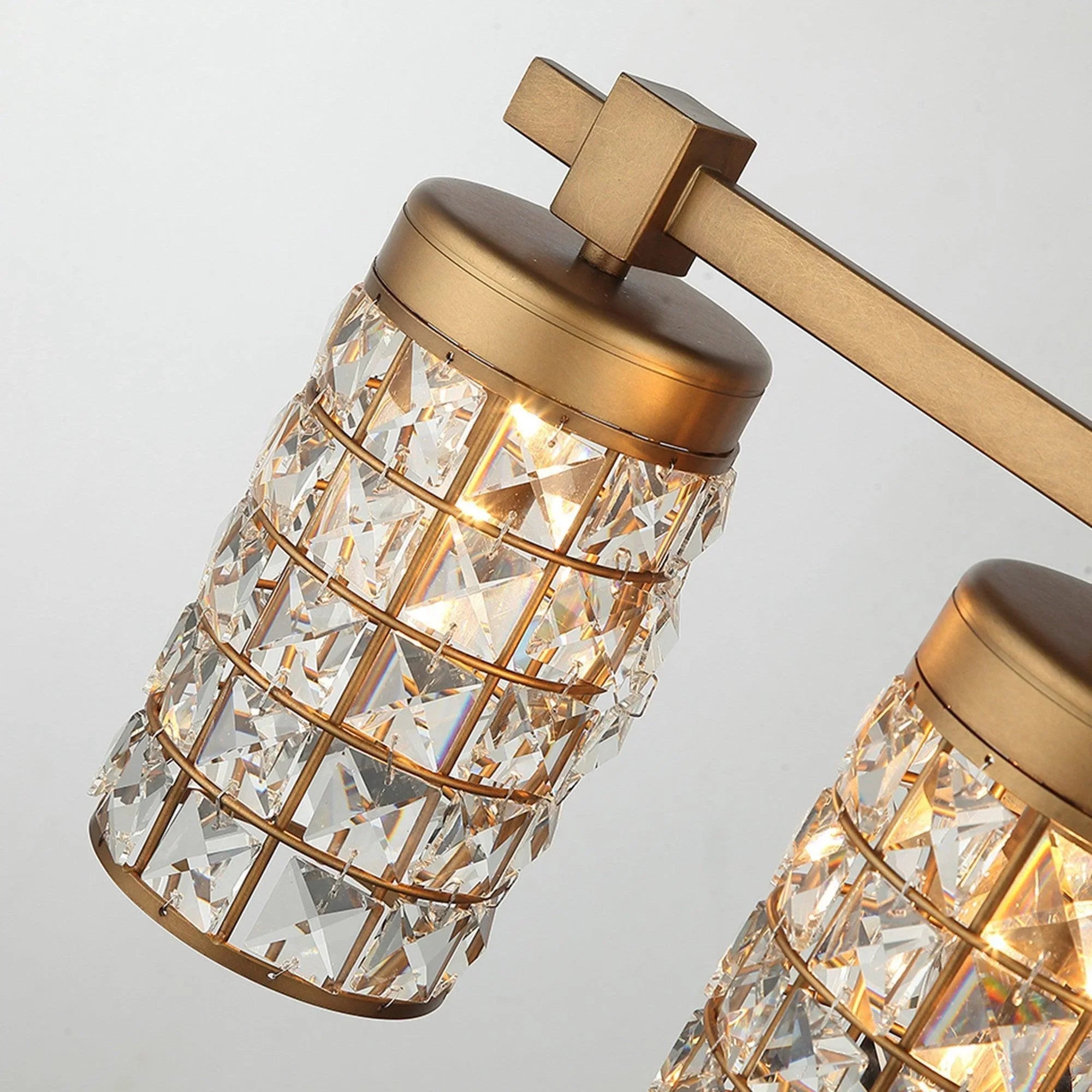 Golden vanity wall sconce showing faceted crystal cylindrical shades and linear mounting bar