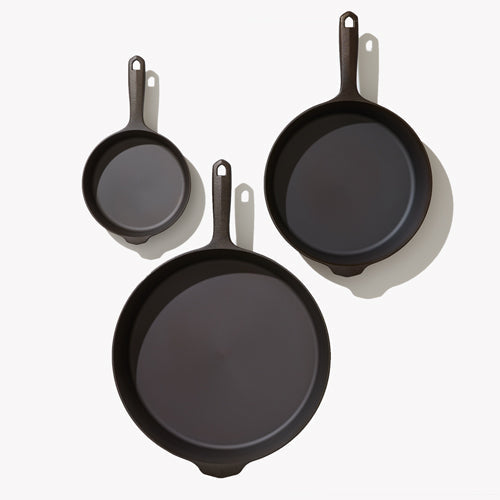 Three-piece cast iron skillet set with dark handles, showing three frying pans