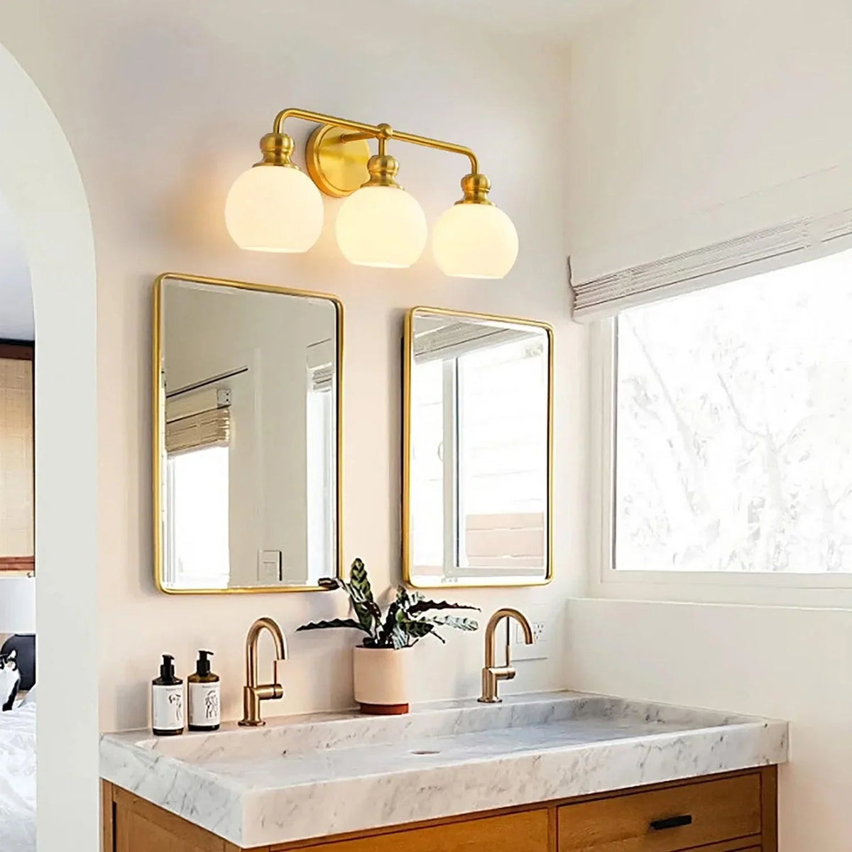Gold 3-light vanity light with three frosted glass dome shades above sink