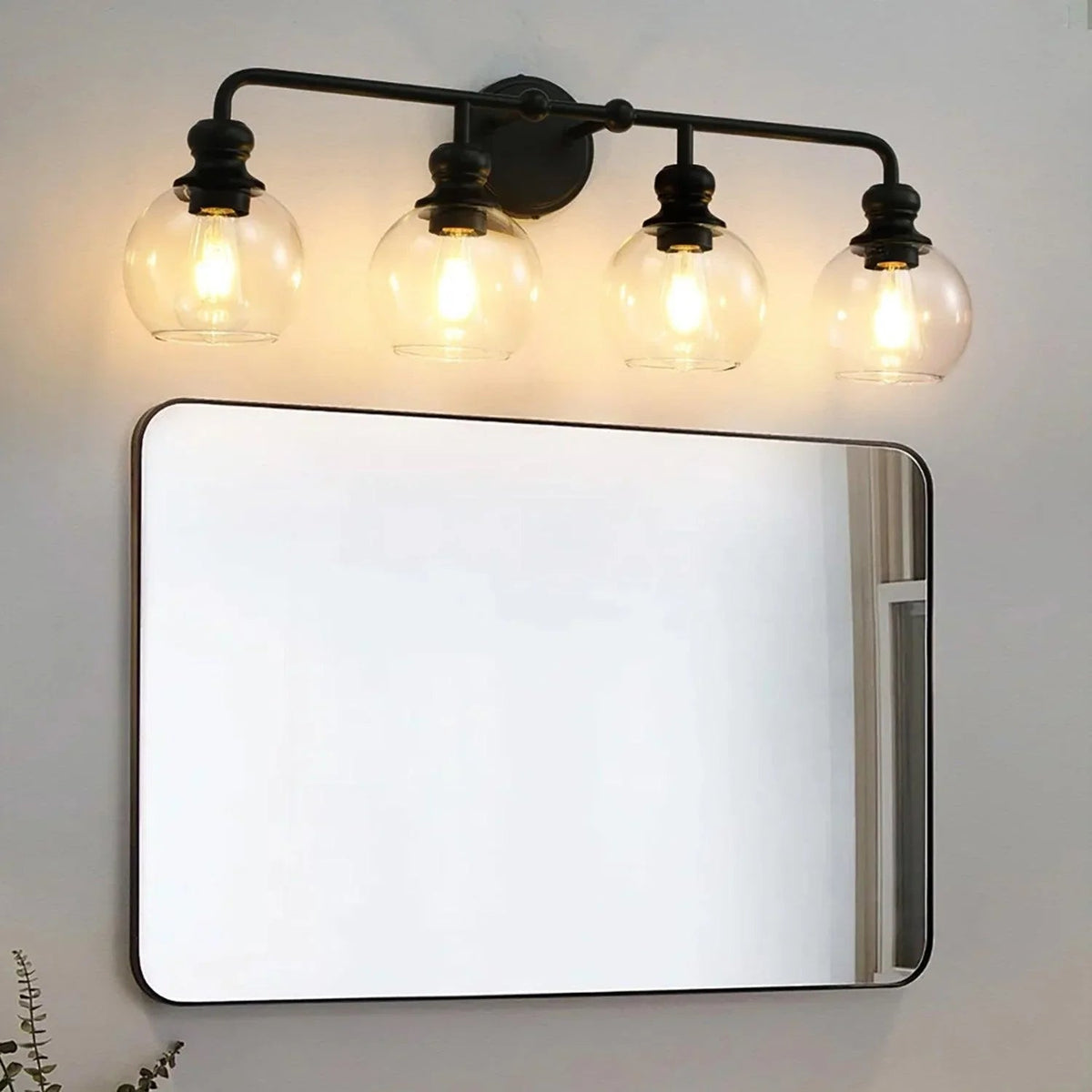 Black 4-light vanity light with clear glass shades and exposed bulbs on a wall mount.
