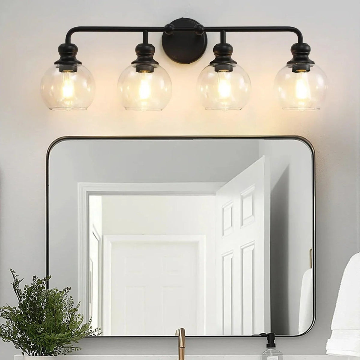 Black 4-light vanity light with four clear glass shades mounted above a large mirror.