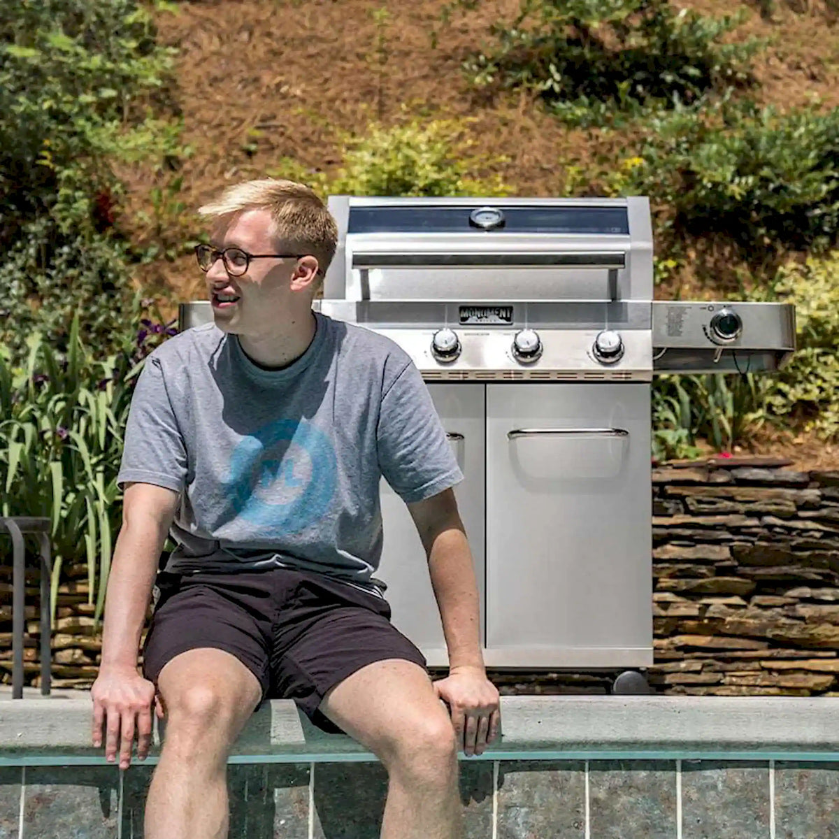 Stainless steel 4-burner propane grill on patio with two cabinet doors