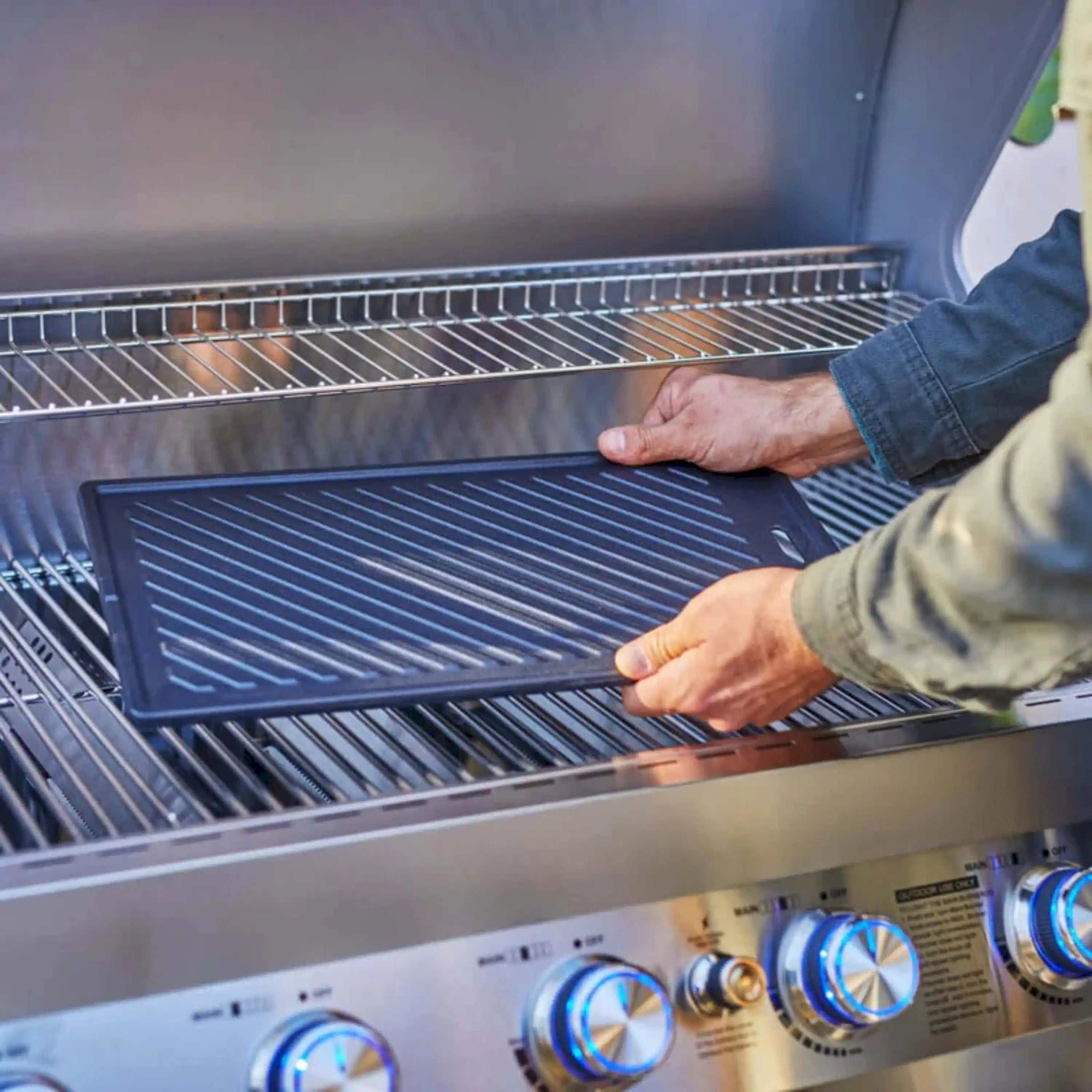 Cast iron reversible cooking plate on a gas grill, with ridged surface under hands