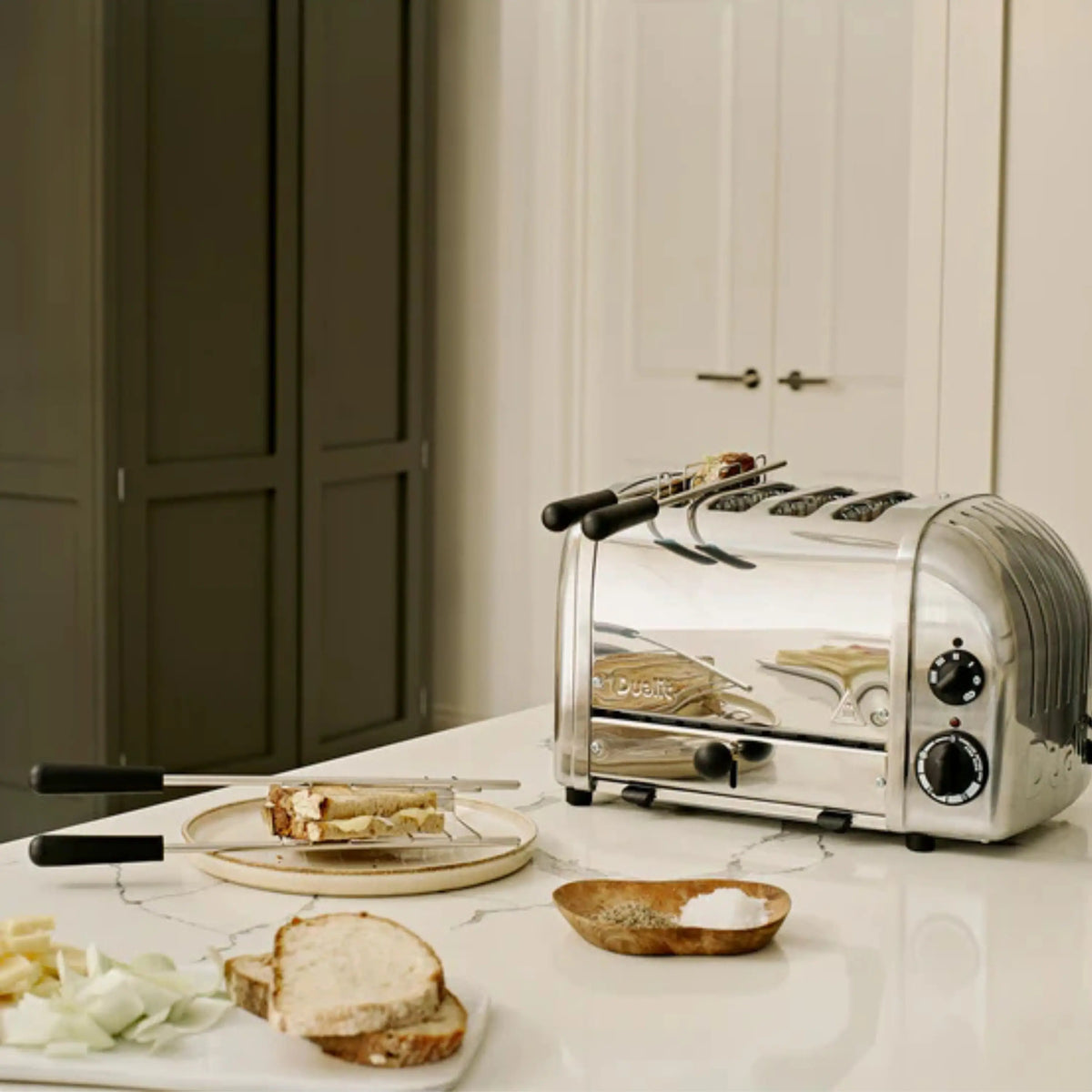 Chrome sandwich toaster on kitchen counter with plate of sandwiches and ingredients nearby
