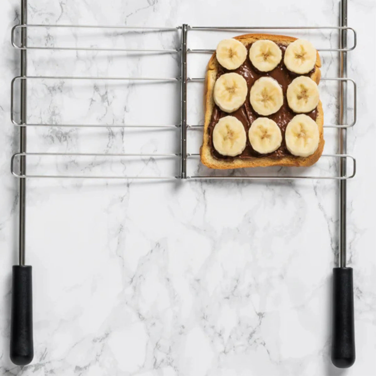 Square bread on grill tray topped with banana slices on open sandwich toaster rack