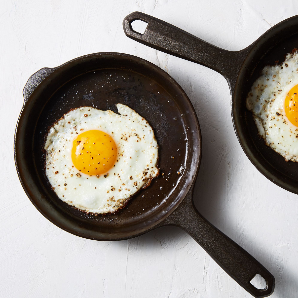 Cast iron skillet with two fried eggs, short side handles, dark cooking surface