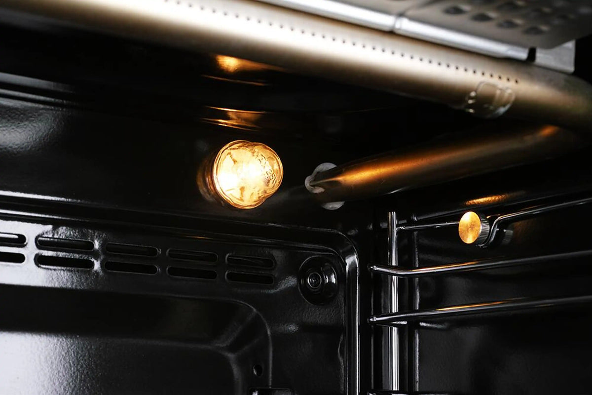 Stainless steel oven cavity with interior light glowing and broiler vent at top