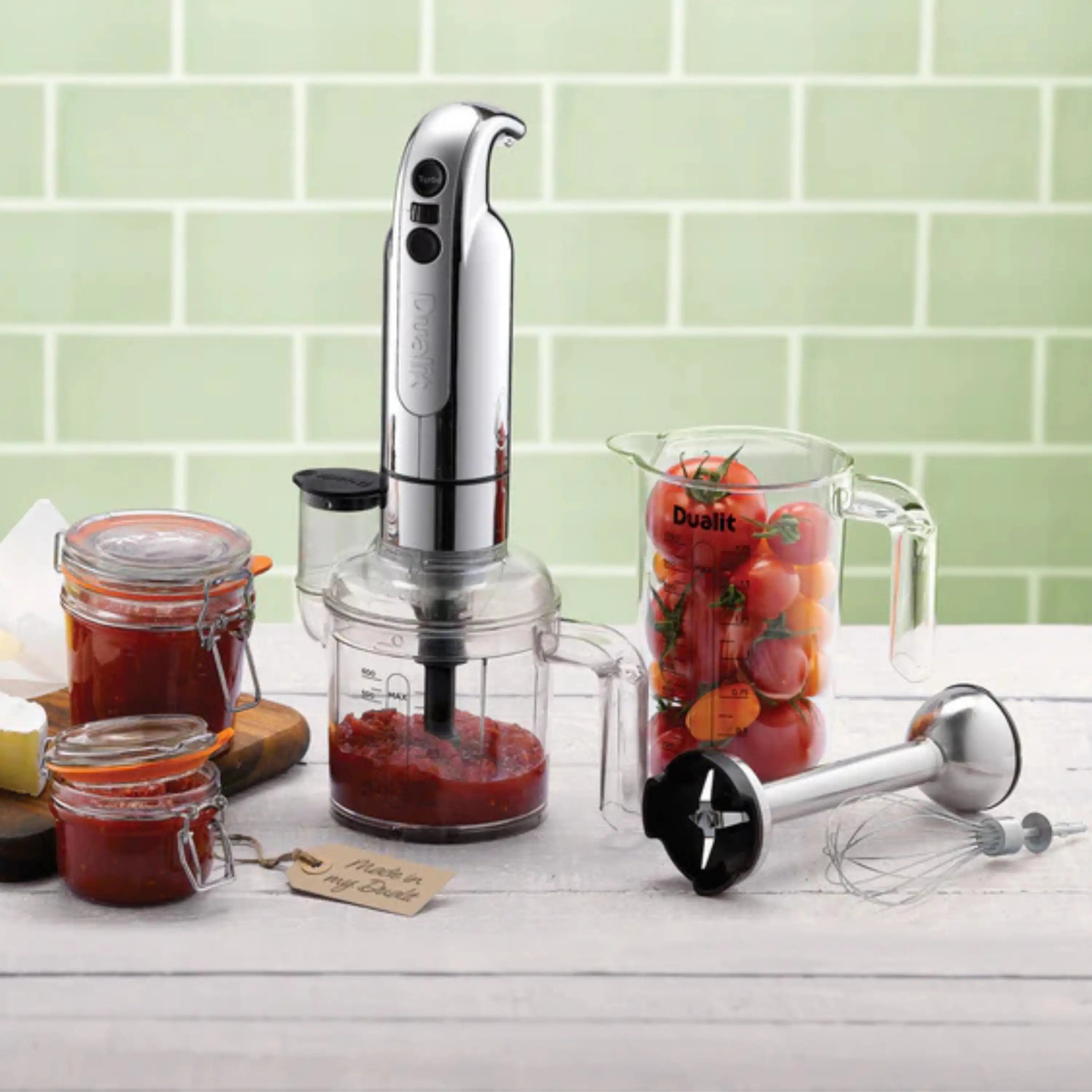 Dualit chrome hand blender with blending cup and beaker set on countertop