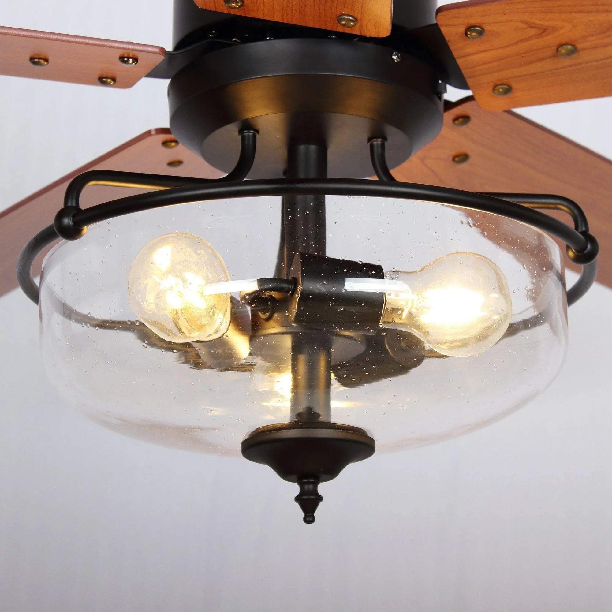 Close-up of black ceiling fan light fixture with four glowing bulbs and glass shade