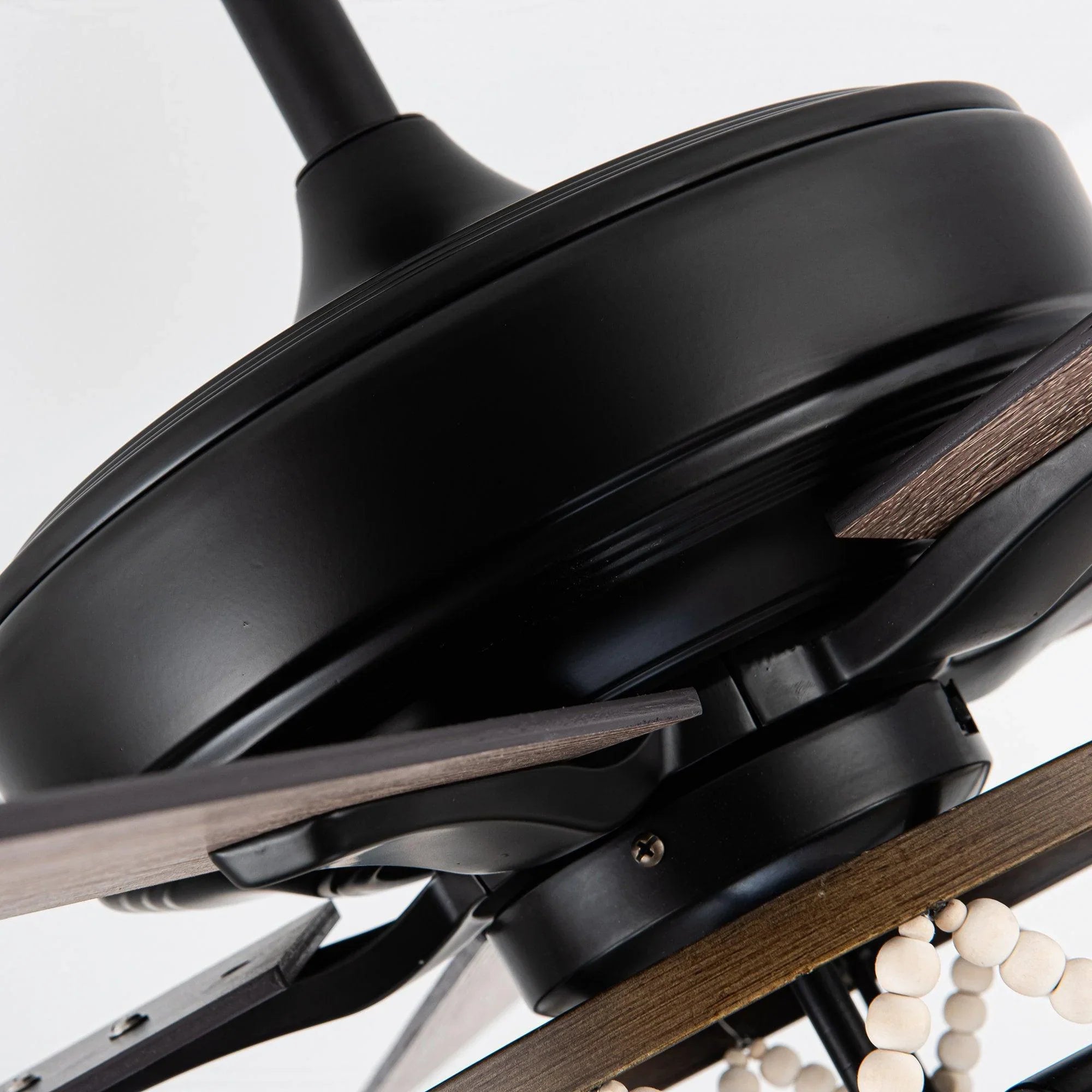 Black ceiling fan motor housing with wood-toned reversible blades near the downrod mount