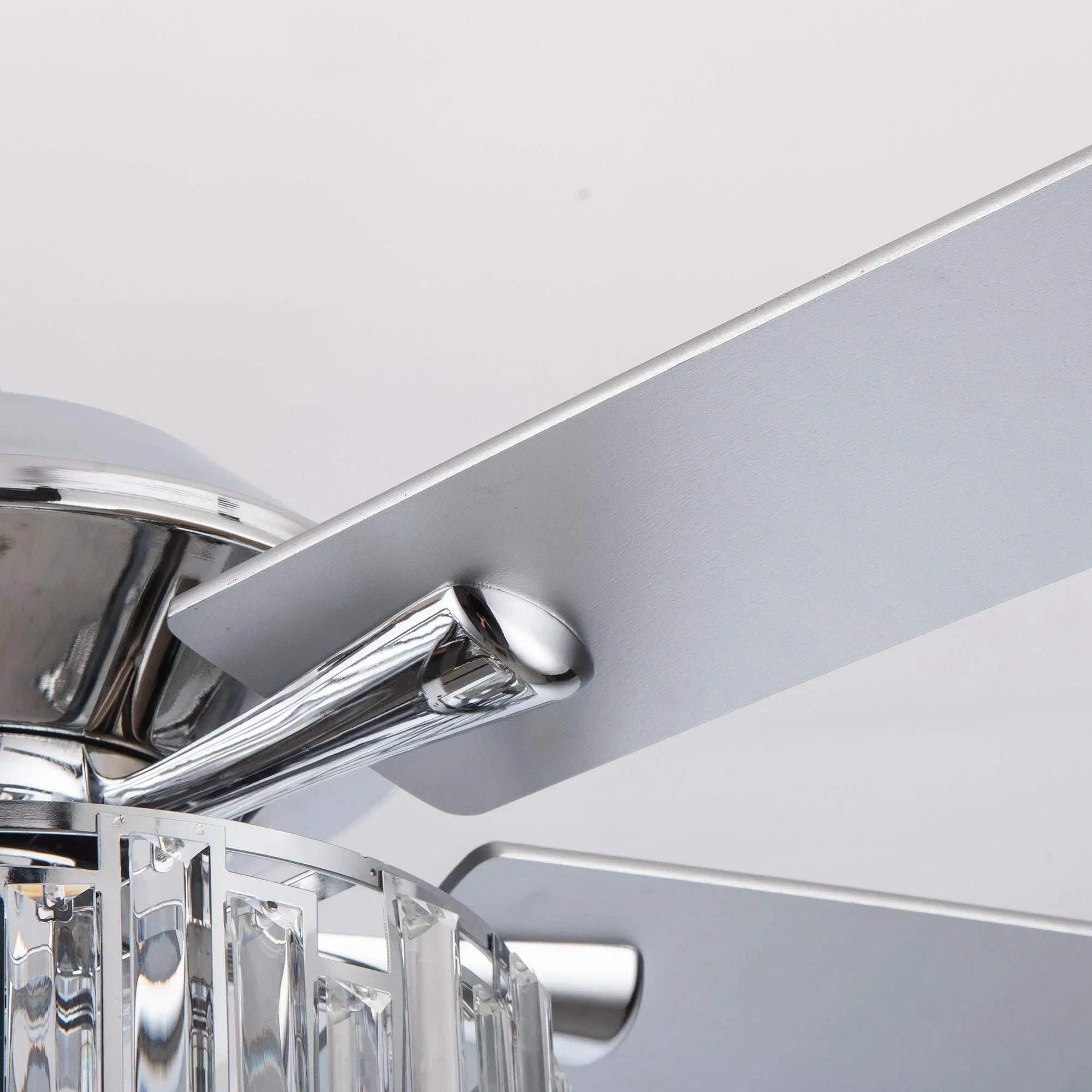 Ceiling fan downrod and chrome bracket detail above crystal light housing.