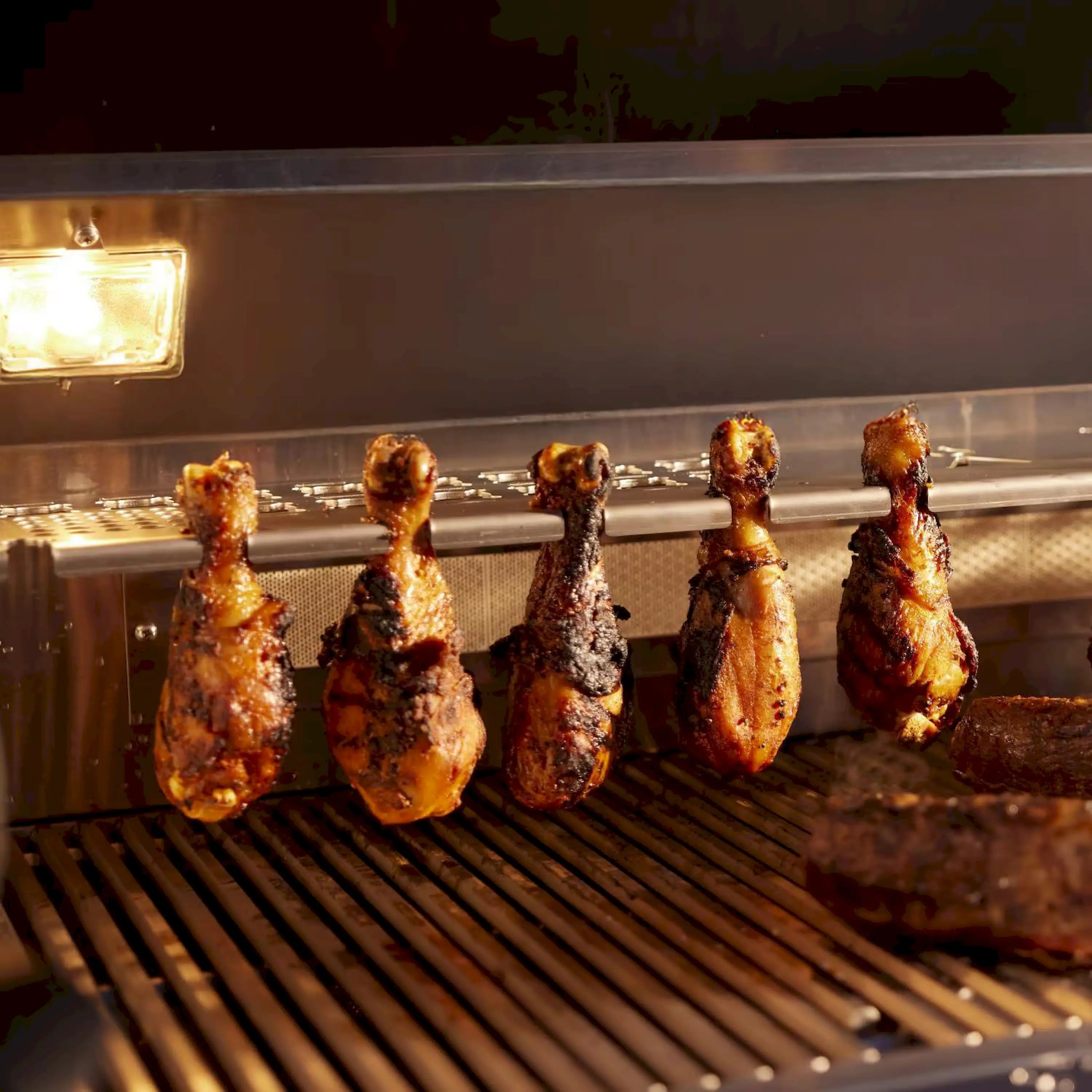 Stainless gas grill with rotisserie-style skewers on rod over glowing burners