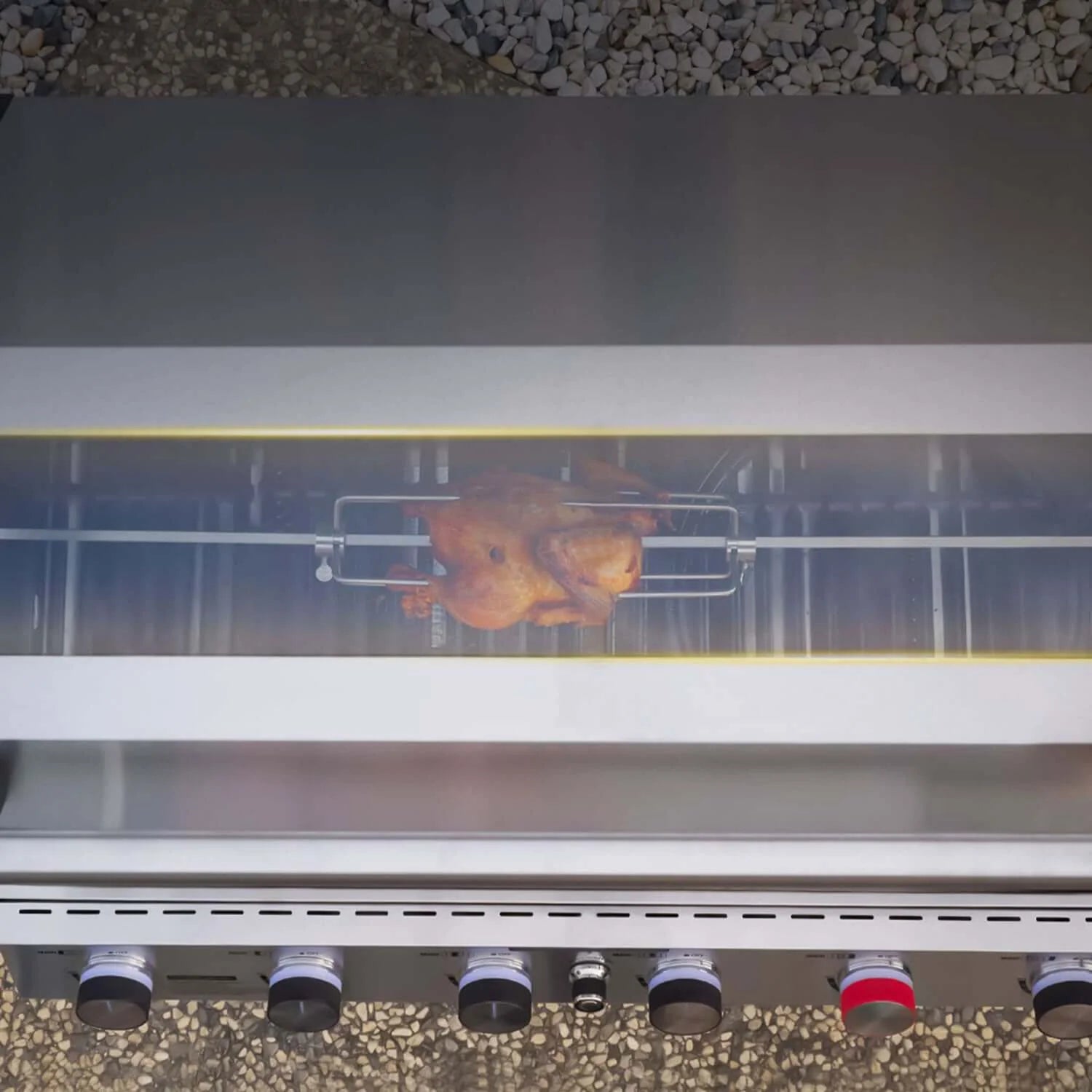 Rotisserie-style chicken on a skewer inside the grill with burner lights glowing
