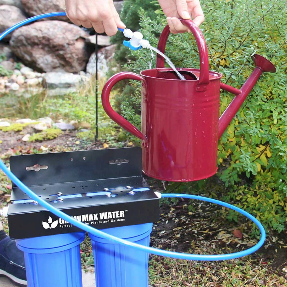 Garden water filtration system connected to a red watering can with blue hoses