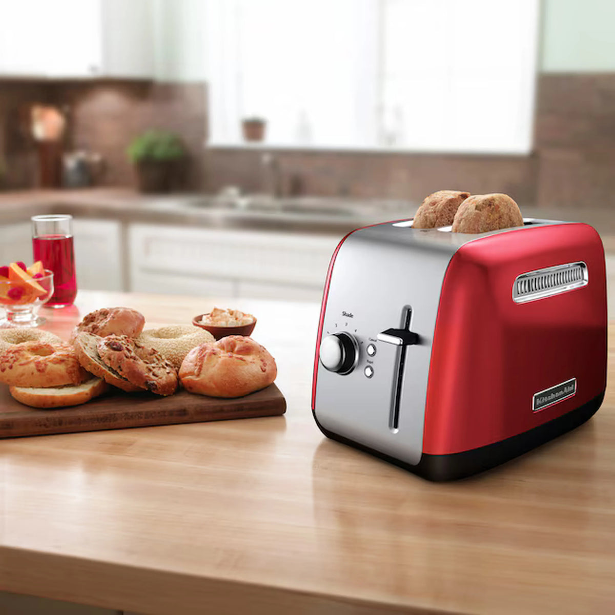 KitchenAid 2-slice toaster in Empire Red on countertop with bread rolls