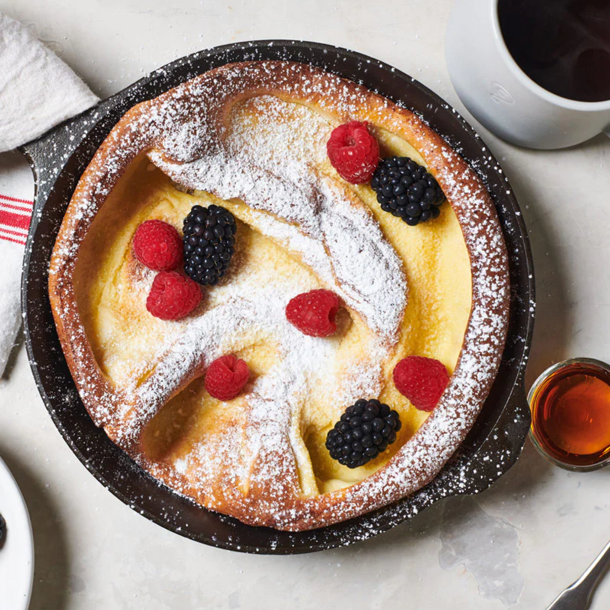 Black cast iron skillet with baked dessert topped with berries and powdered sugar