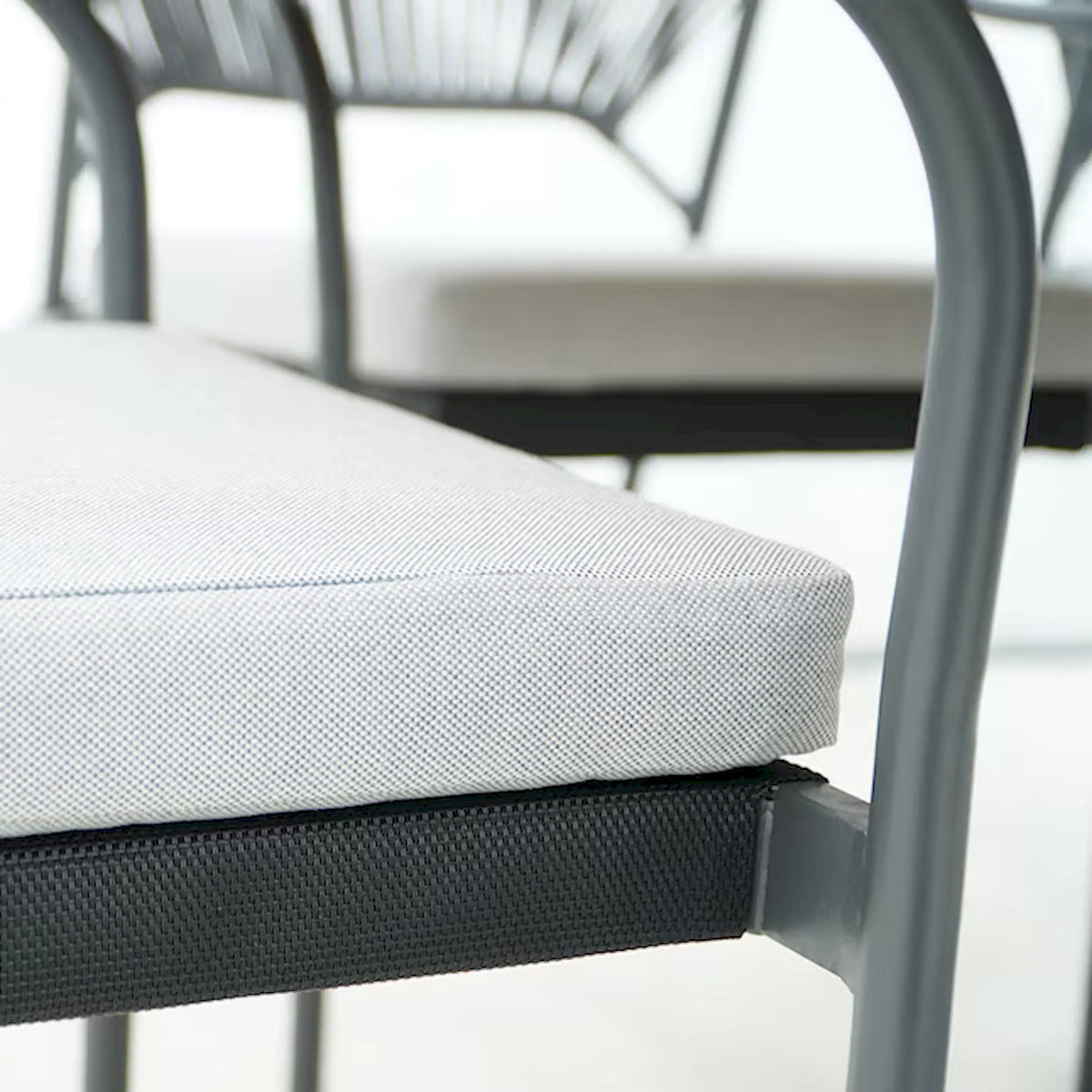 Outdoor dining chair seat cushion on black woven frame, close-up of cushion edge.