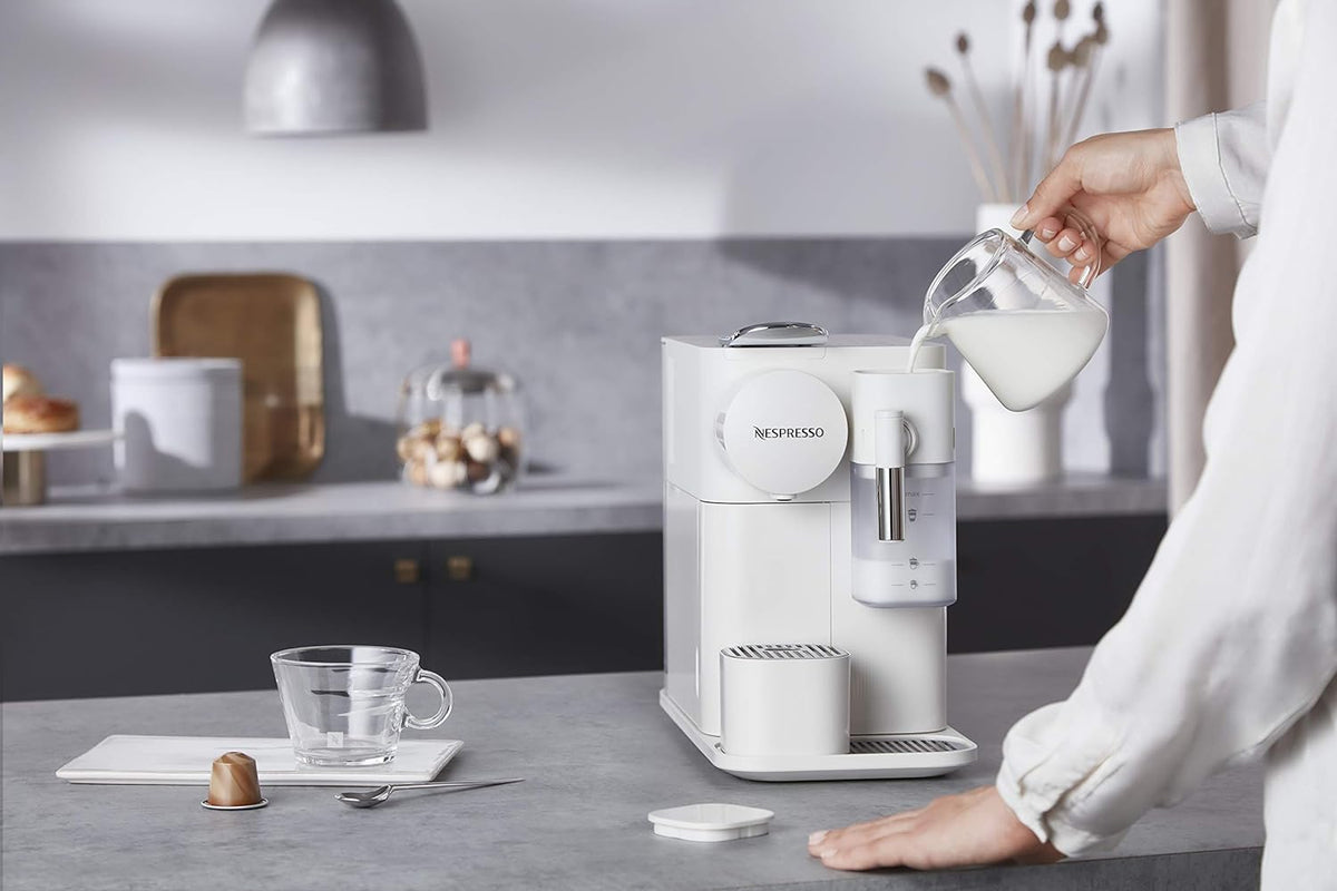 White single-serve Nespresso-style coffee machine with milk frother, pouring into cup
