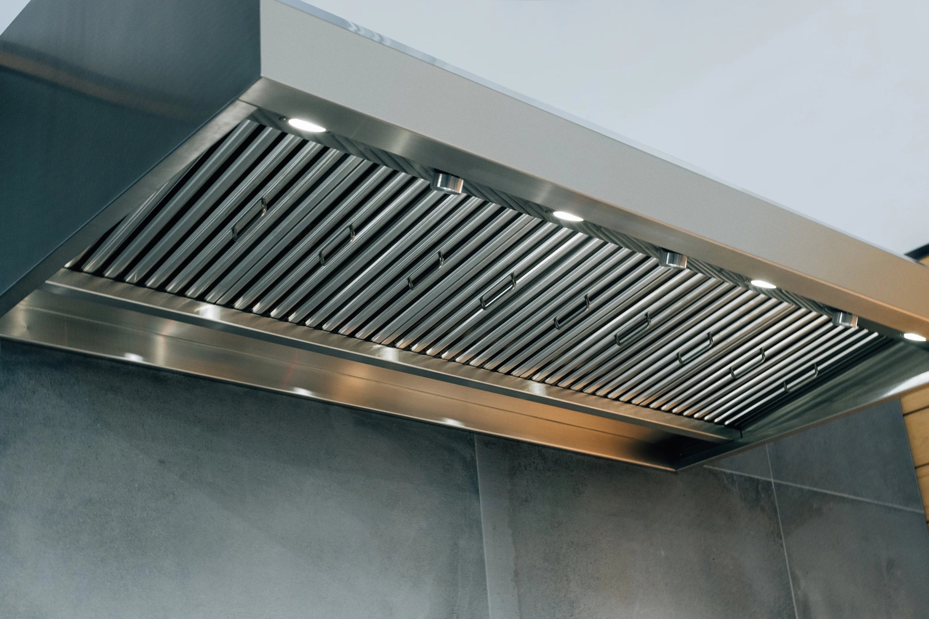 Stainless steel wall vent hood with slatted filter grille and underside lights