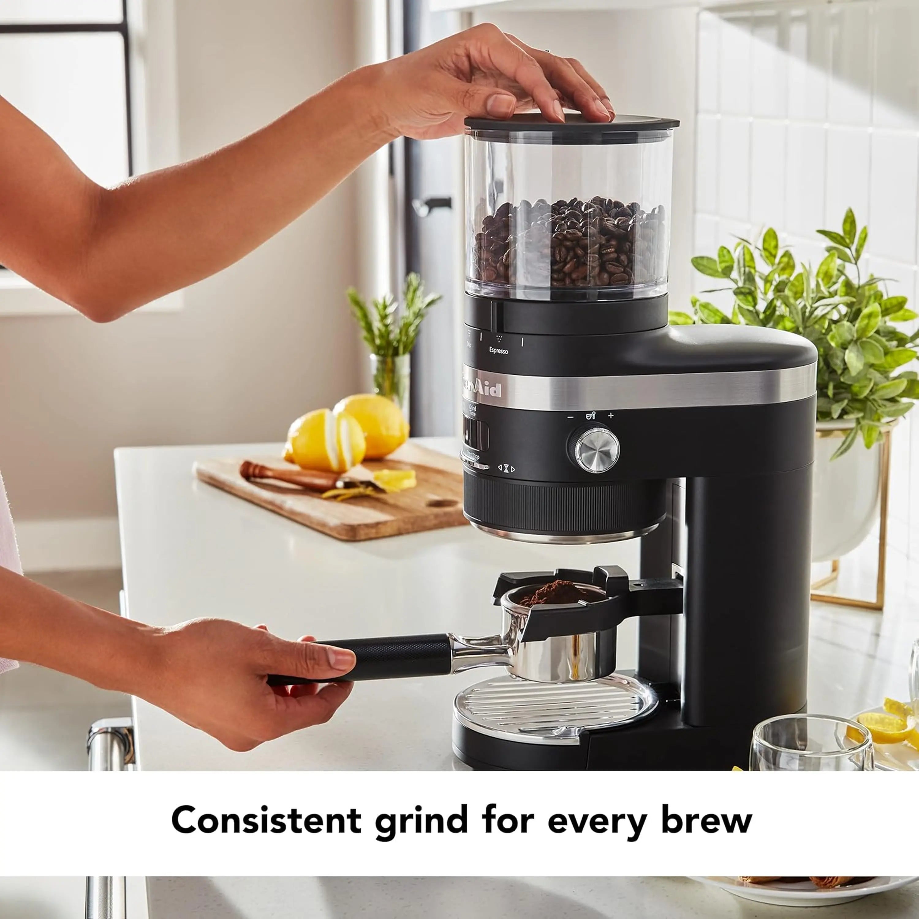 Black matte burr coffee grinder with clear hopper and drip cup, held by hands