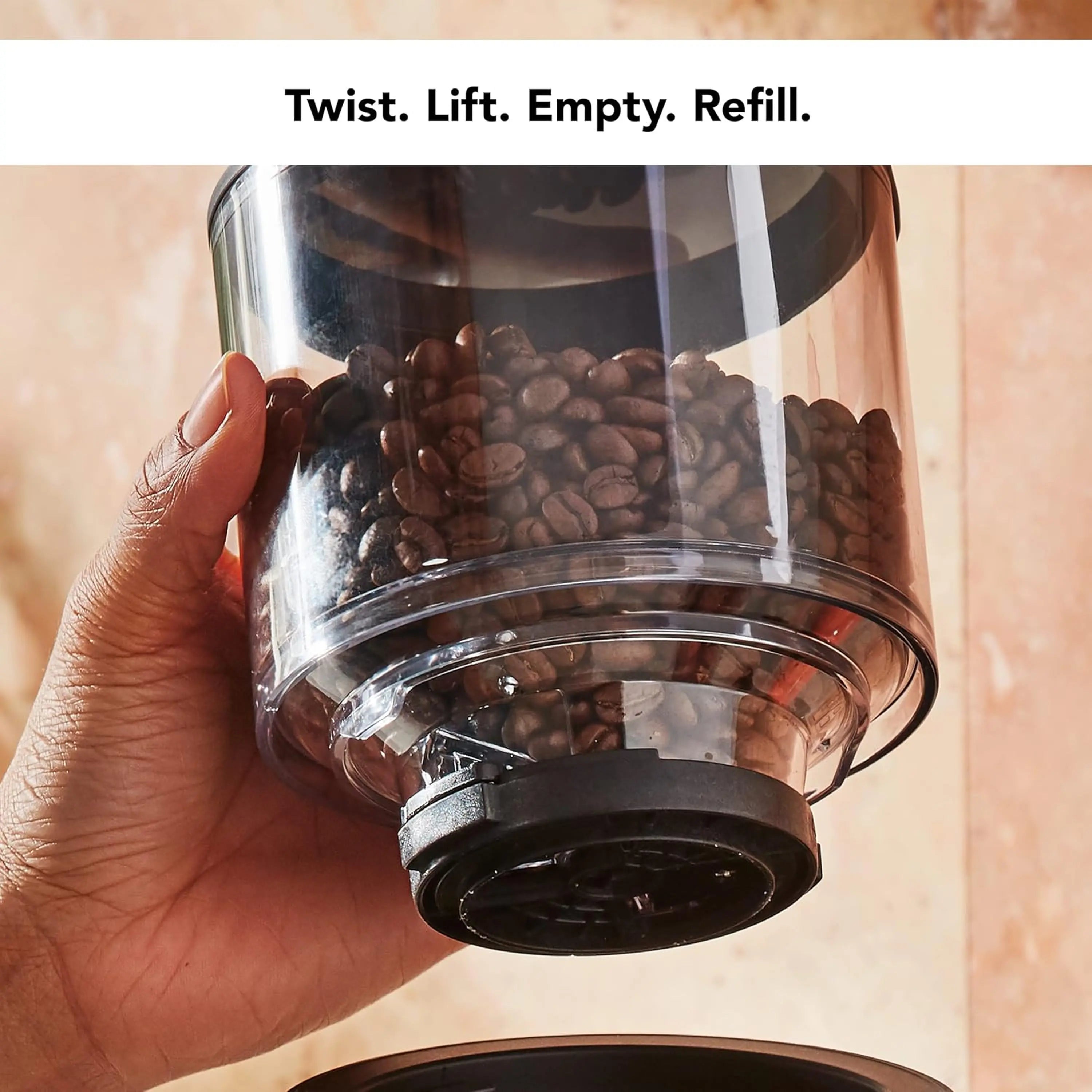 Clear bean hopper held in hand above black matte burr grinder, KitchenAid