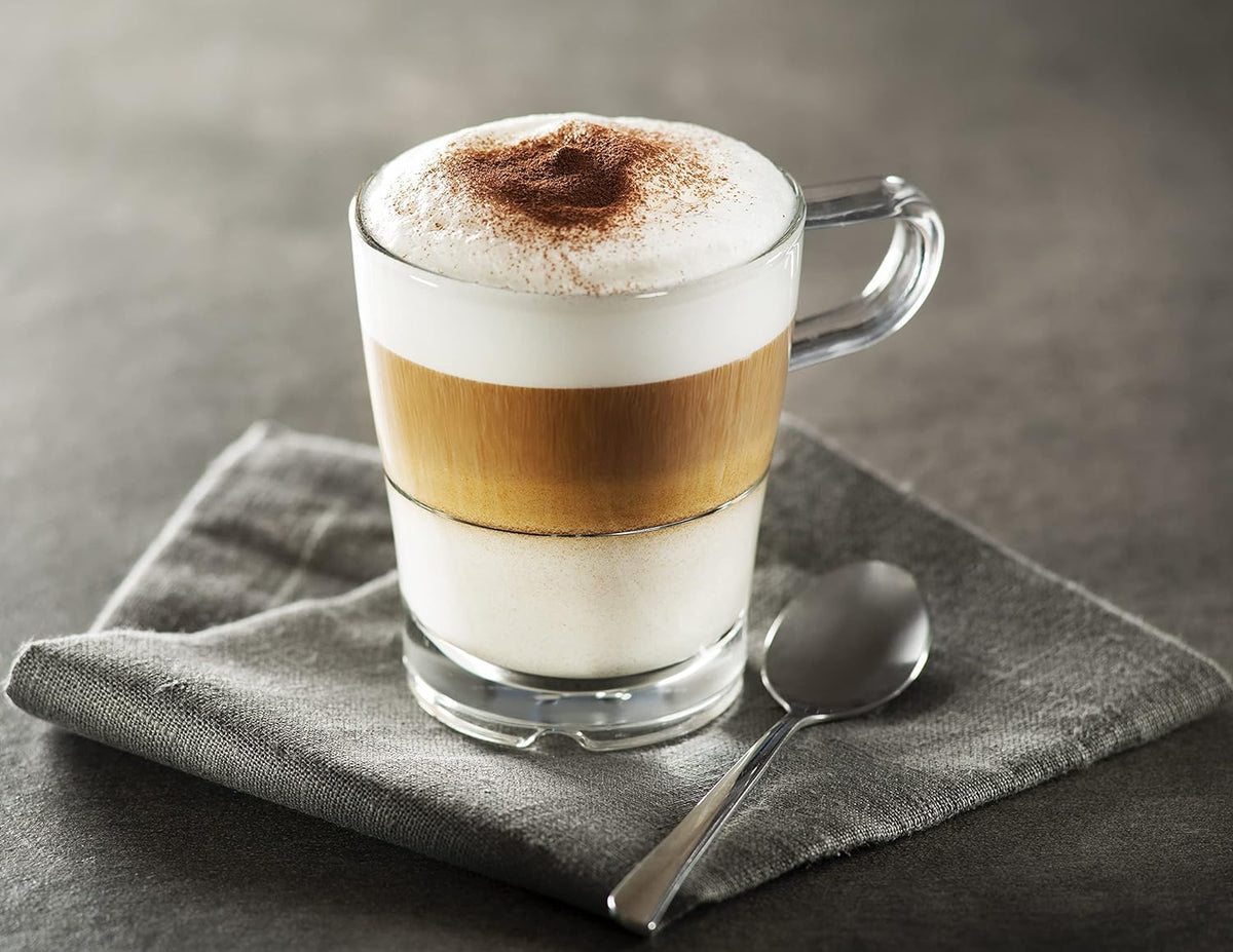 Stainless steel milk frother jug, pouring frothy layered drink into a glass cup