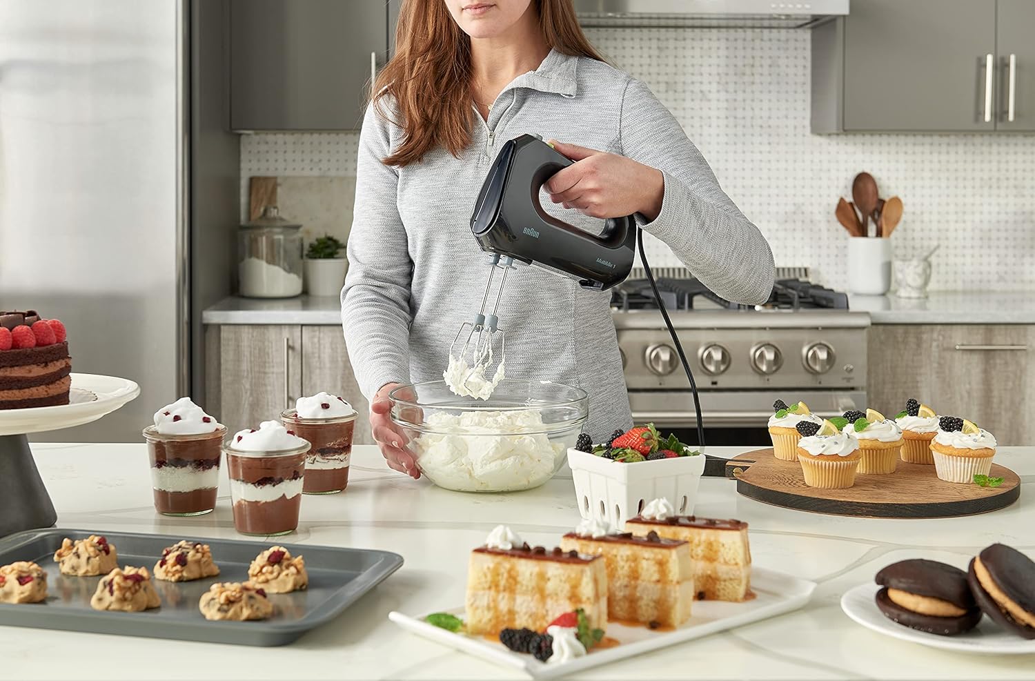 Woman holding a black hand mixer above a glass mixing bowl with beaters