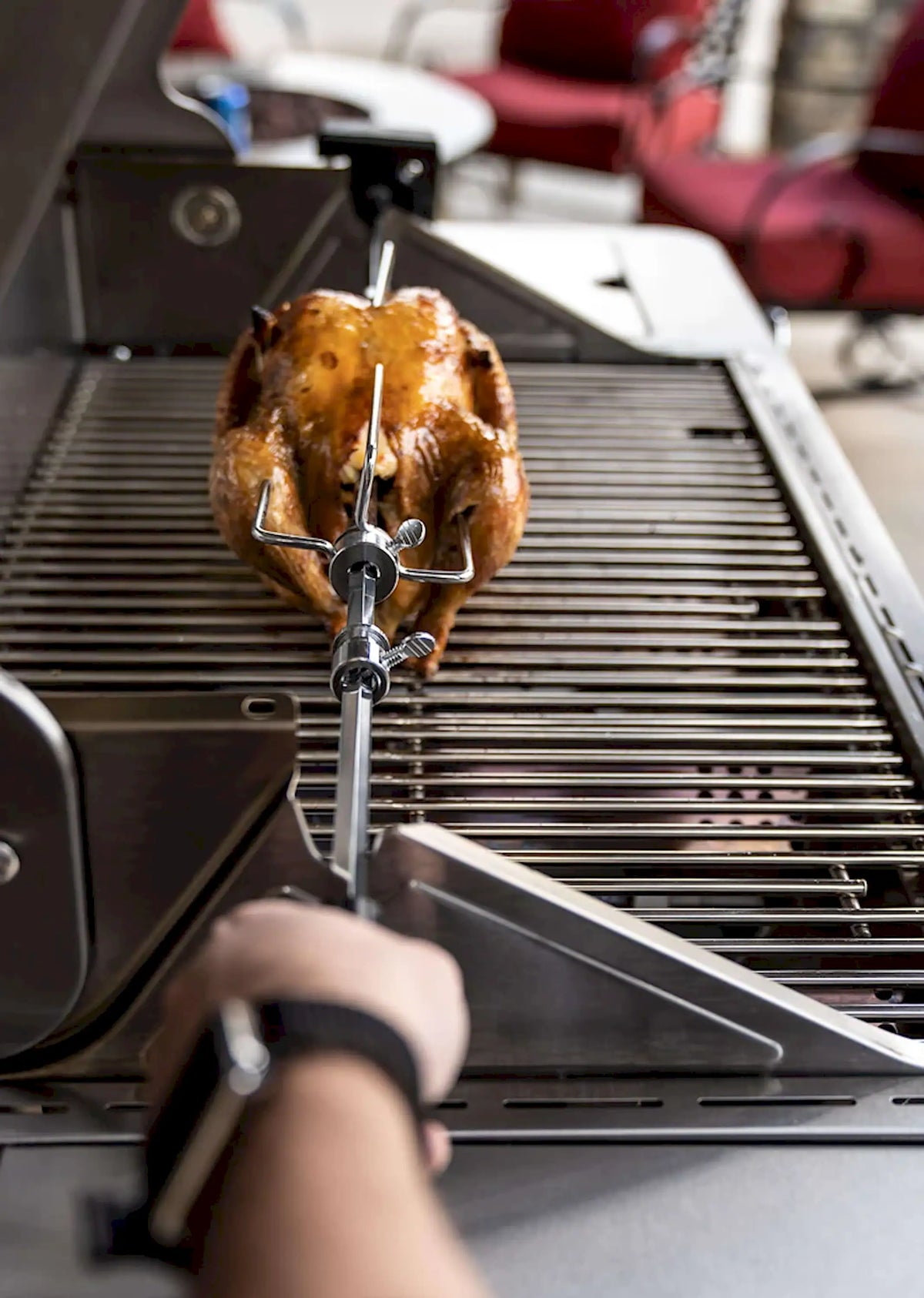 Rotisserie skewer kit holding a whole roasted chicken on grill grates