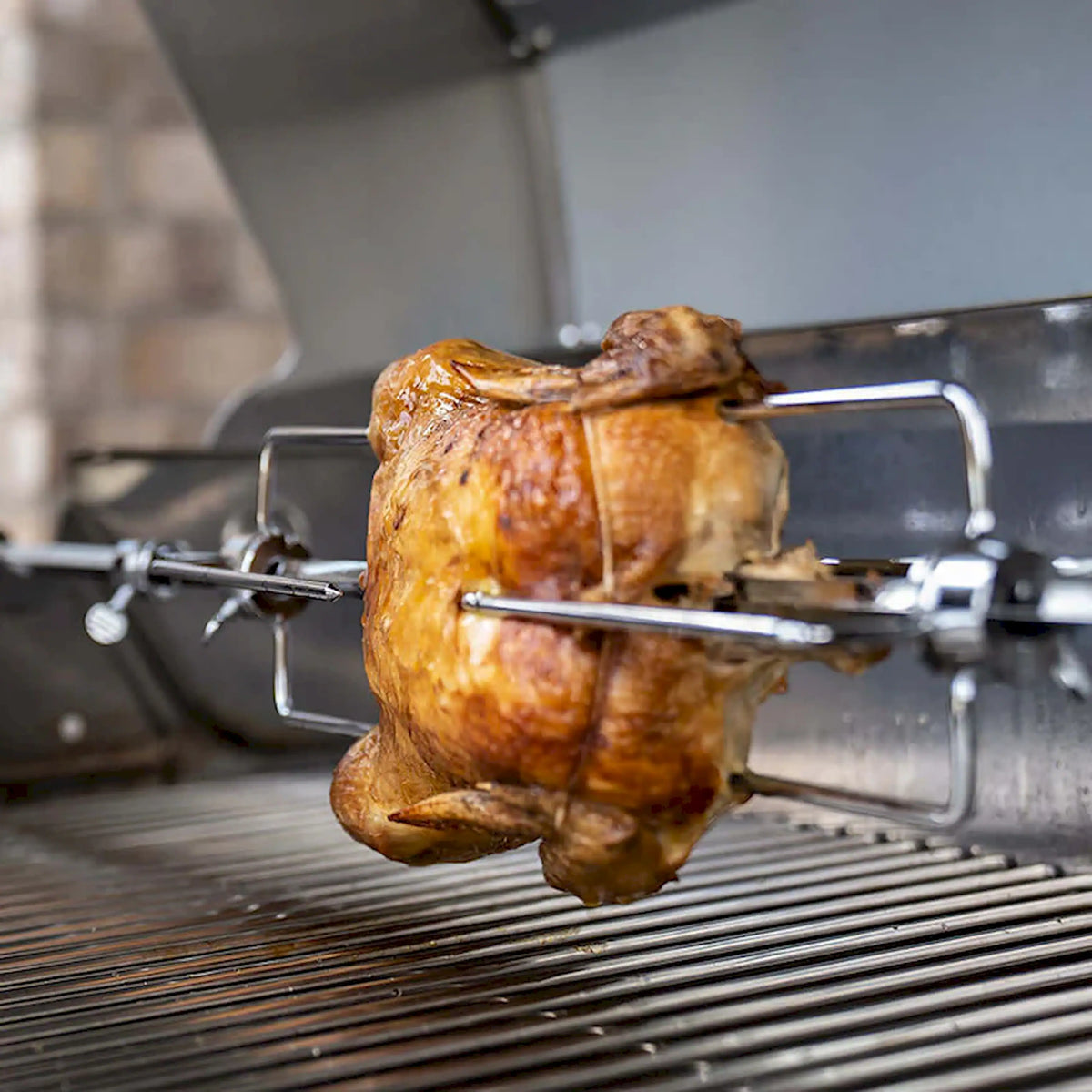 Roasted chicken on rotisserie spit with prongs over grill grates