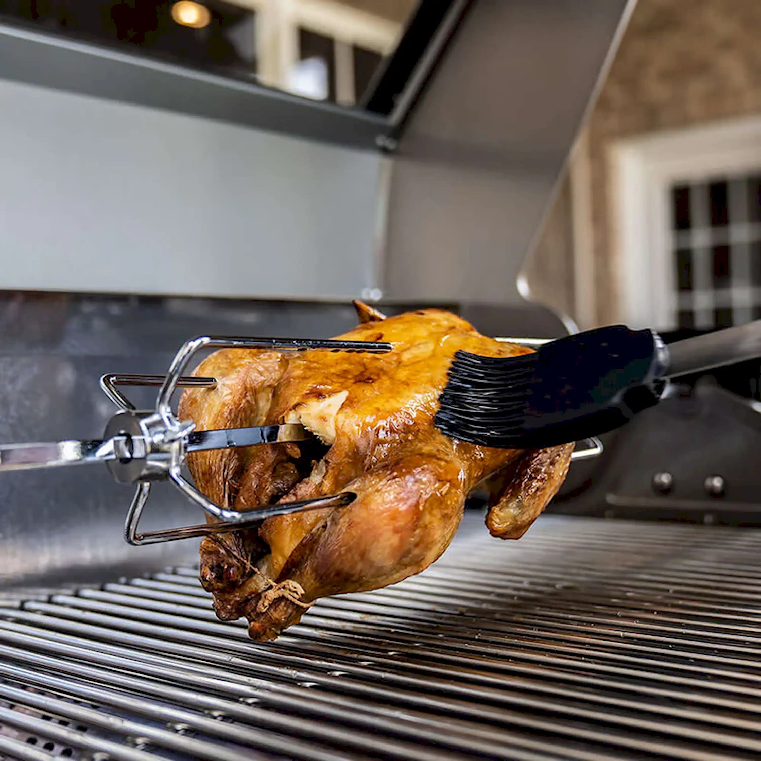 Rotisserie spit with roasted chicken and basting brush on grill grates