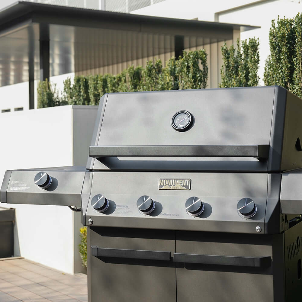 Black propane gas grill with lid, control knobs, and Monument logo on front panel