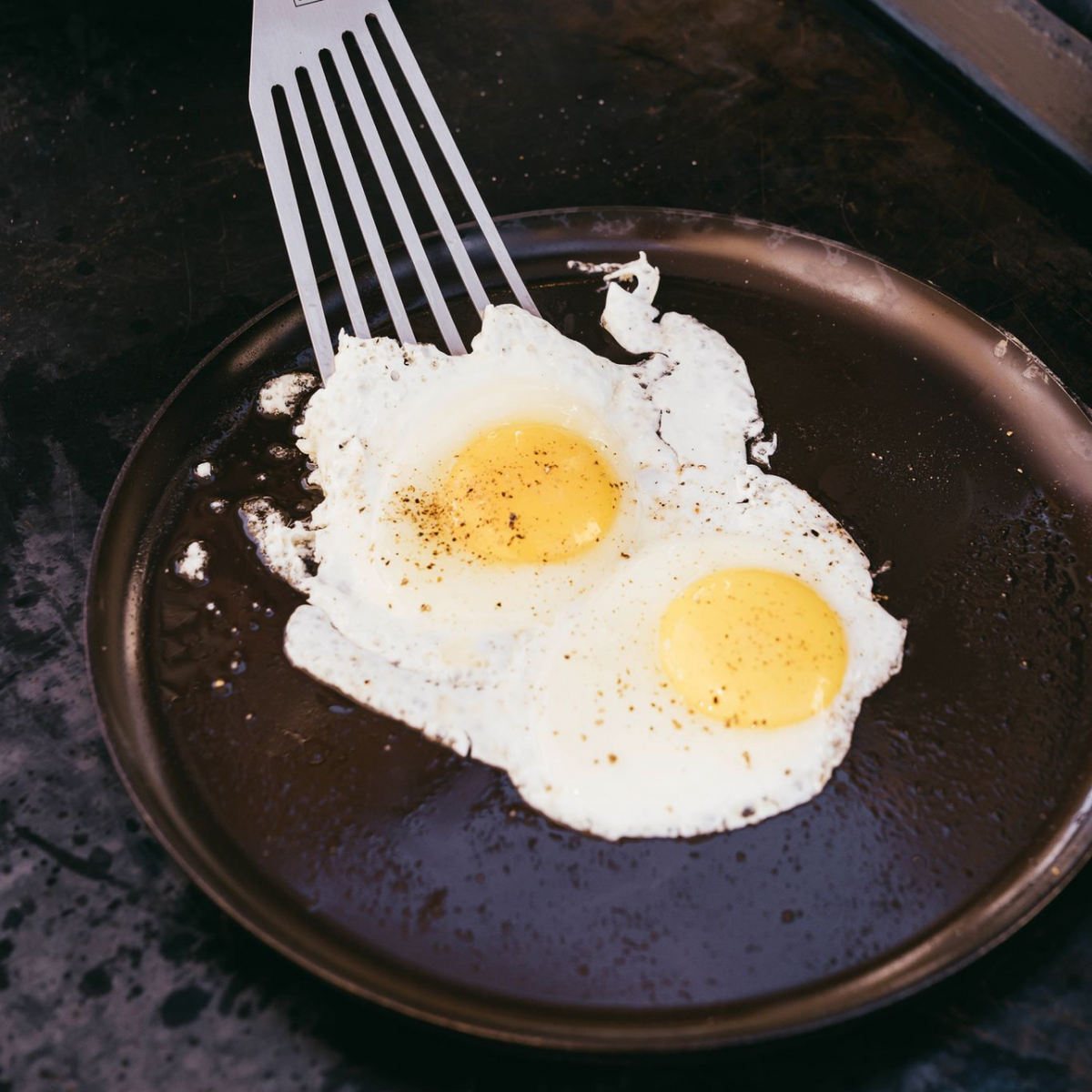 Round cast iron griddle with two fried eggs and metal spatula