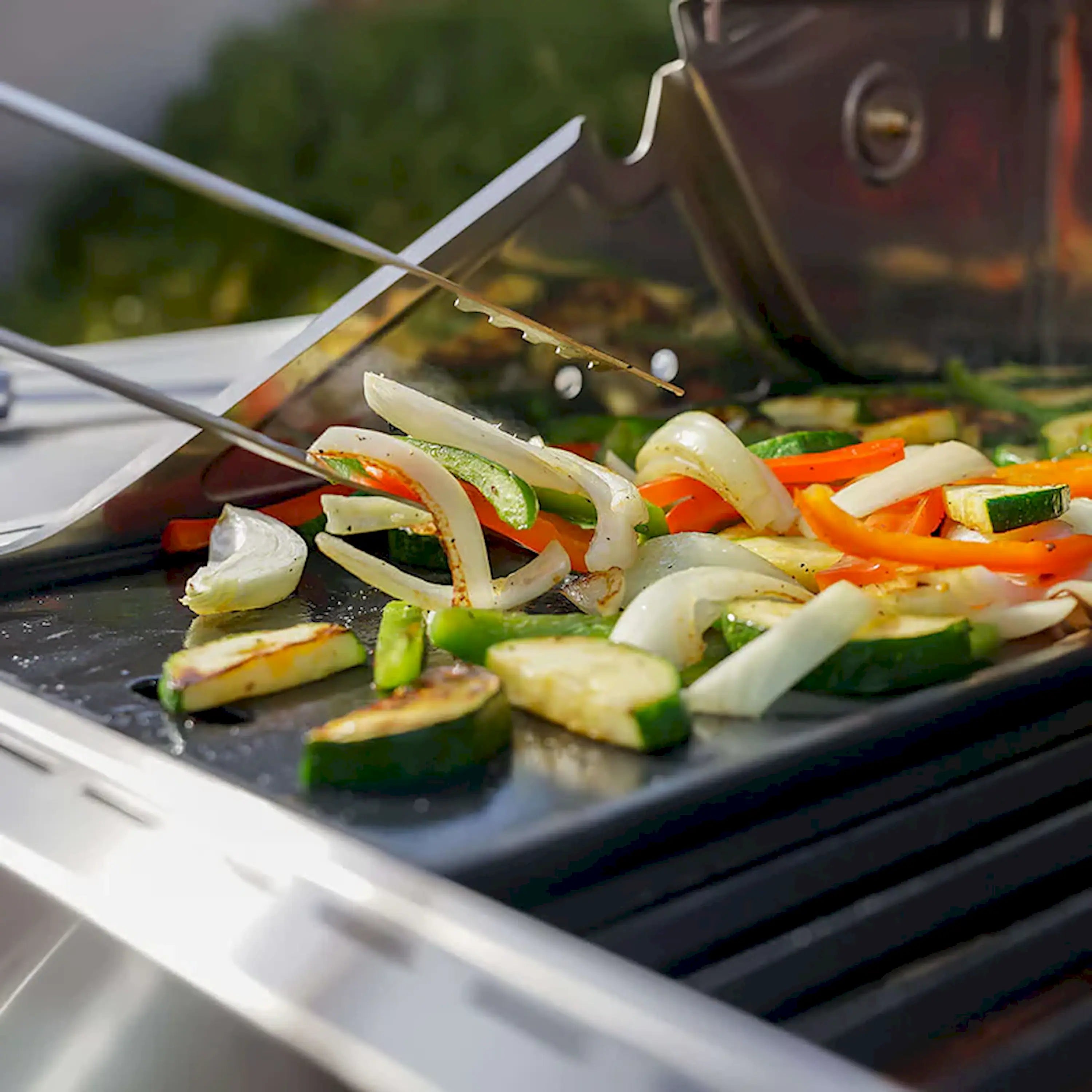 Open grill lid with vegetables sizzling on dark cooking grates