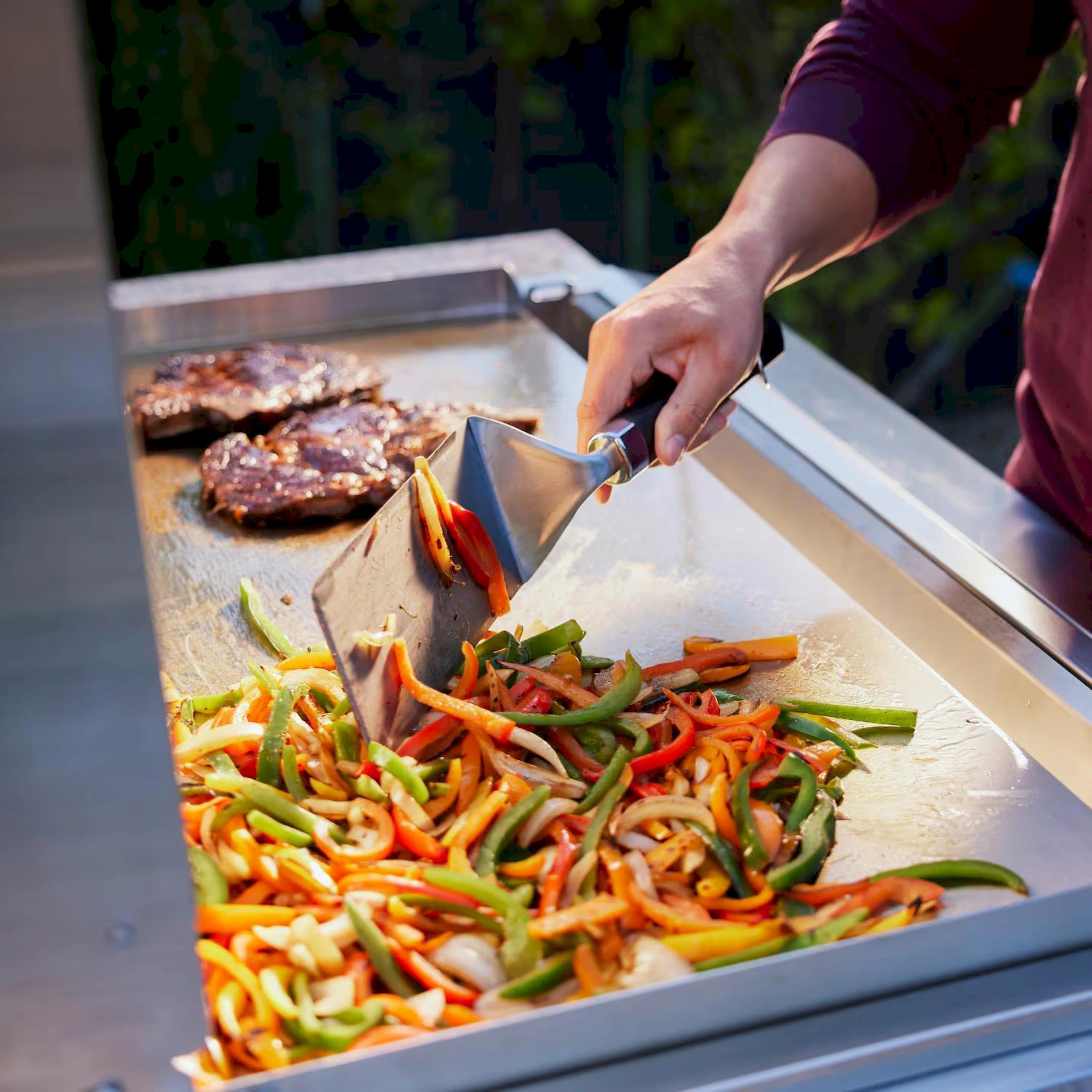 Stainless steel griddle cooking vegetables with hand lifting a spatula