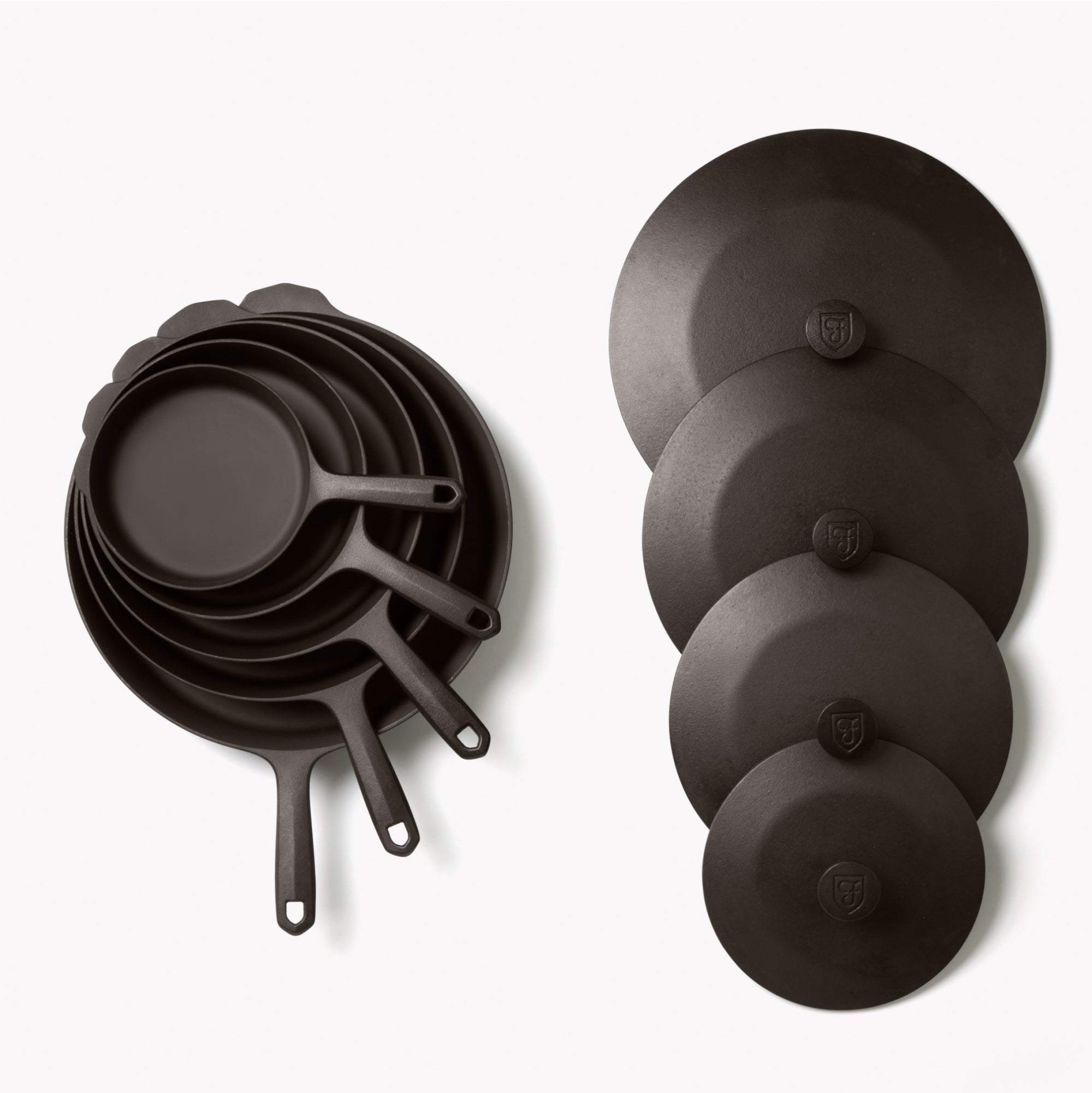 Stack of dark cast iron skillets with short loop handles and two lids