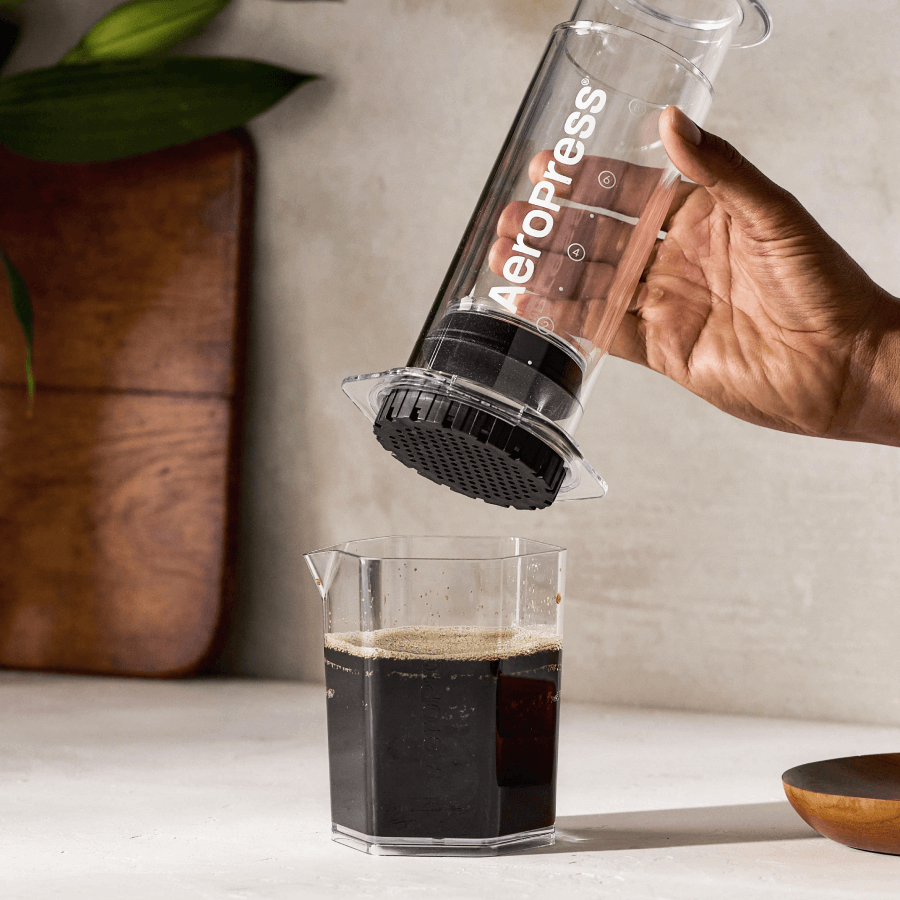 Hand tilting clear XL coffee maker, pouring dark coffee into a glass cup