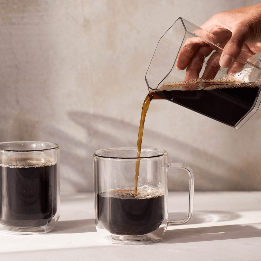 Clear XL coffee maker pouring dark coffee into a glass mug
