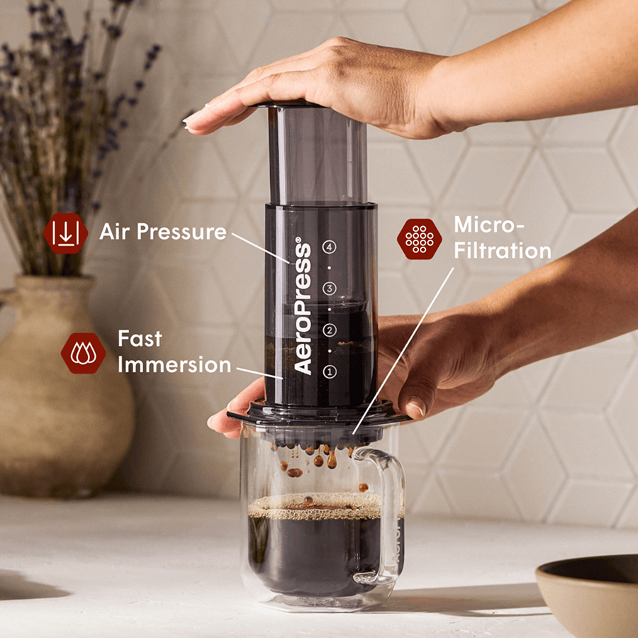 Black AeroPress coffee maker with plunger chamber, positioned above a glass mug