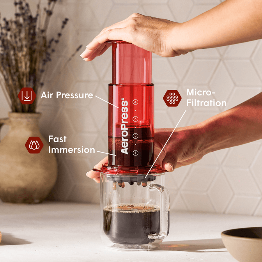 Red AeroPress coffee maker with plunger chamber and filter cap, brewing over a glass mug