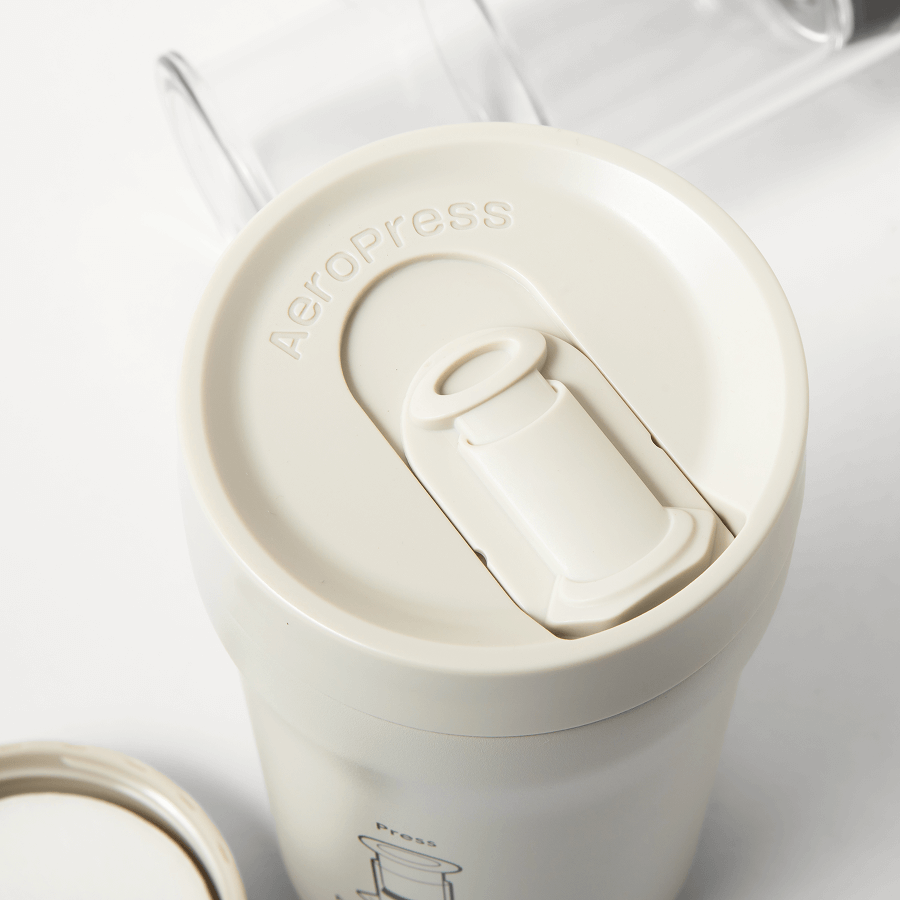 Cream travel coffee tumbler with top brew chamber and plunger assembly inside