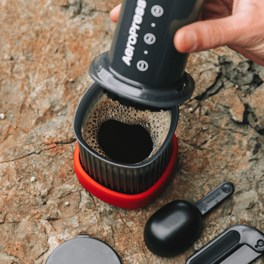 AeroPress brewing cup with coffee grounds steeping, plus scoop and lid