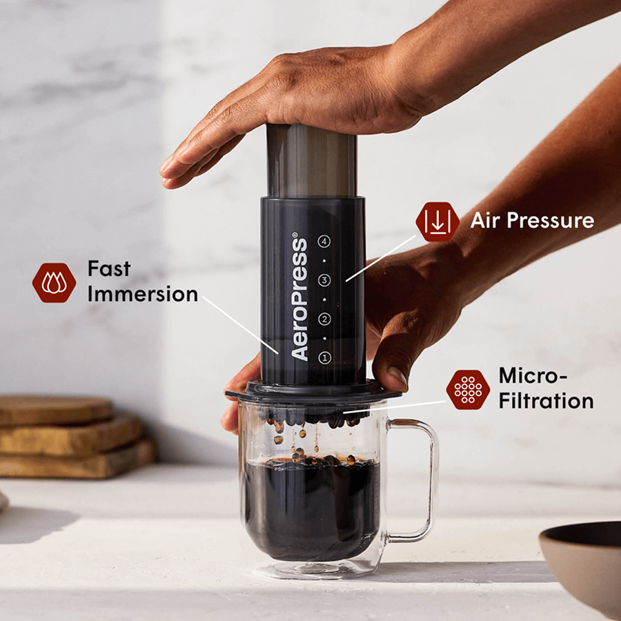 AeroPress coffee maker being pressed over a glass mug with dark coffee